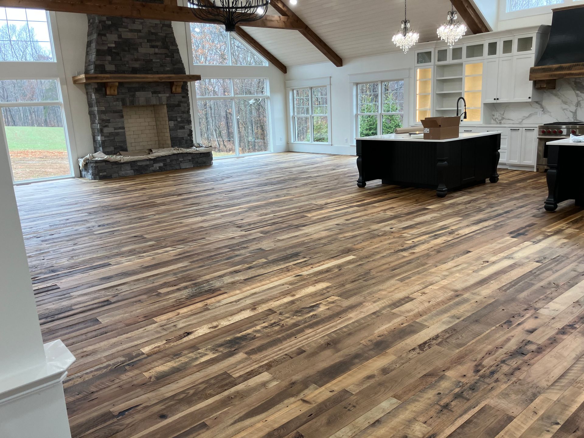 Spacious lodge-style room with wood floors, stone fireplace, and large windows with a bar area in back