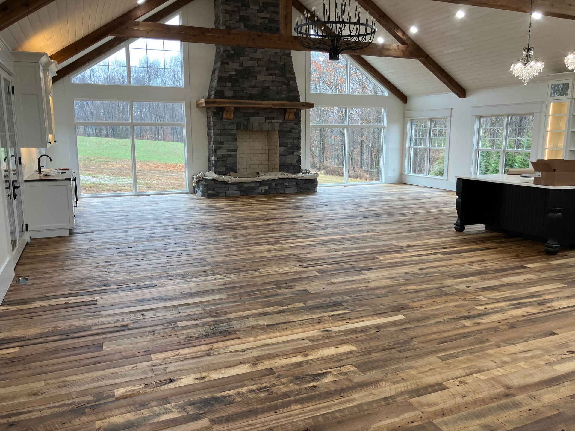 Spacious rustic living room with wood floors, stone fireplace, exposed beams, and large windows