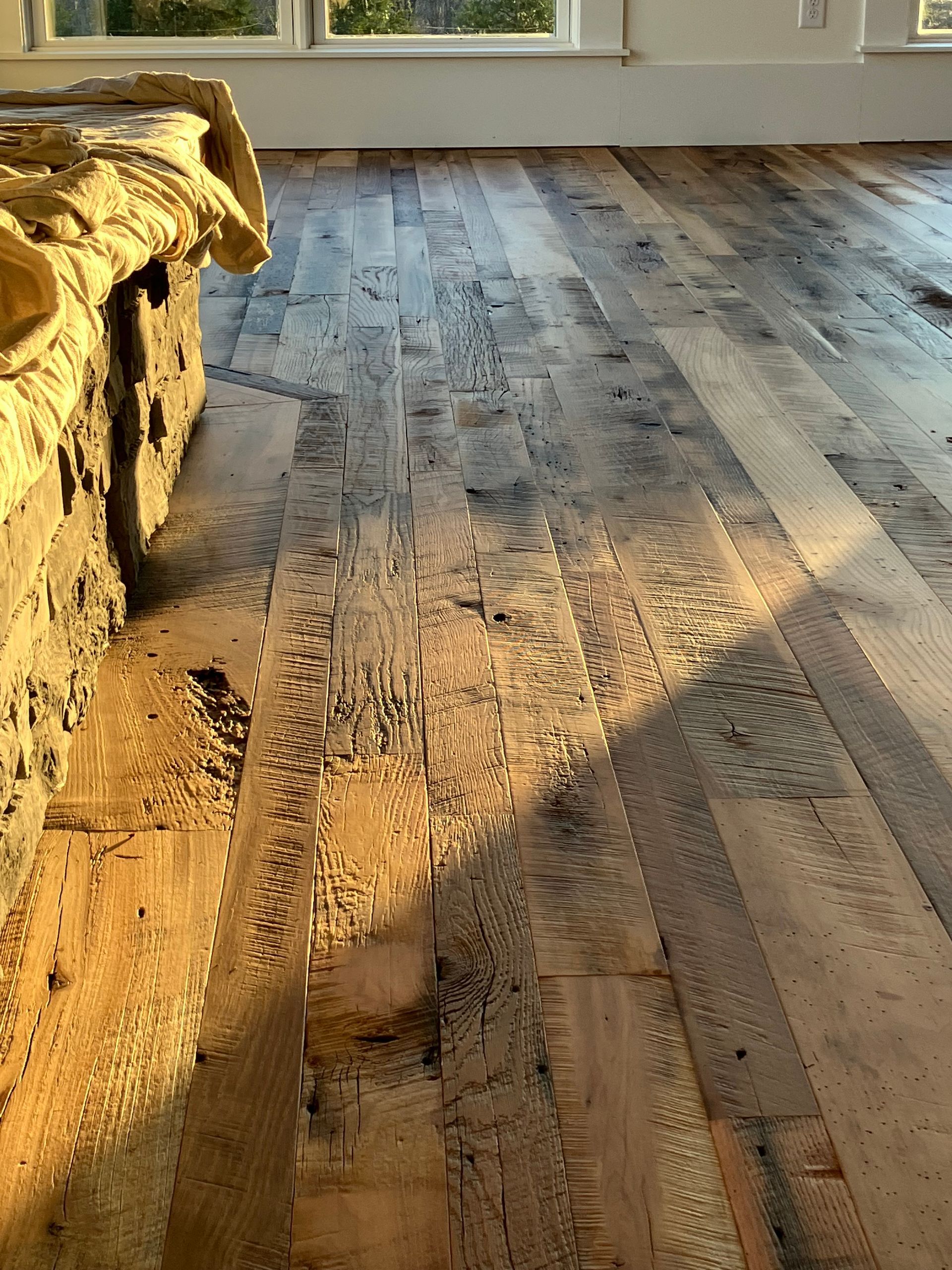 Sunlit rustic wooden floor by a window, with a yellow couch at left and long shadows across the room
