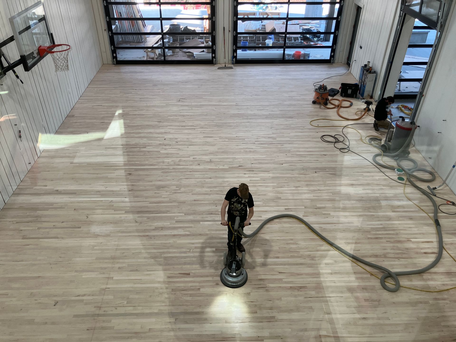 Floor buffer cleaning a large empty showroom with light wood flooring and garage doors in the background