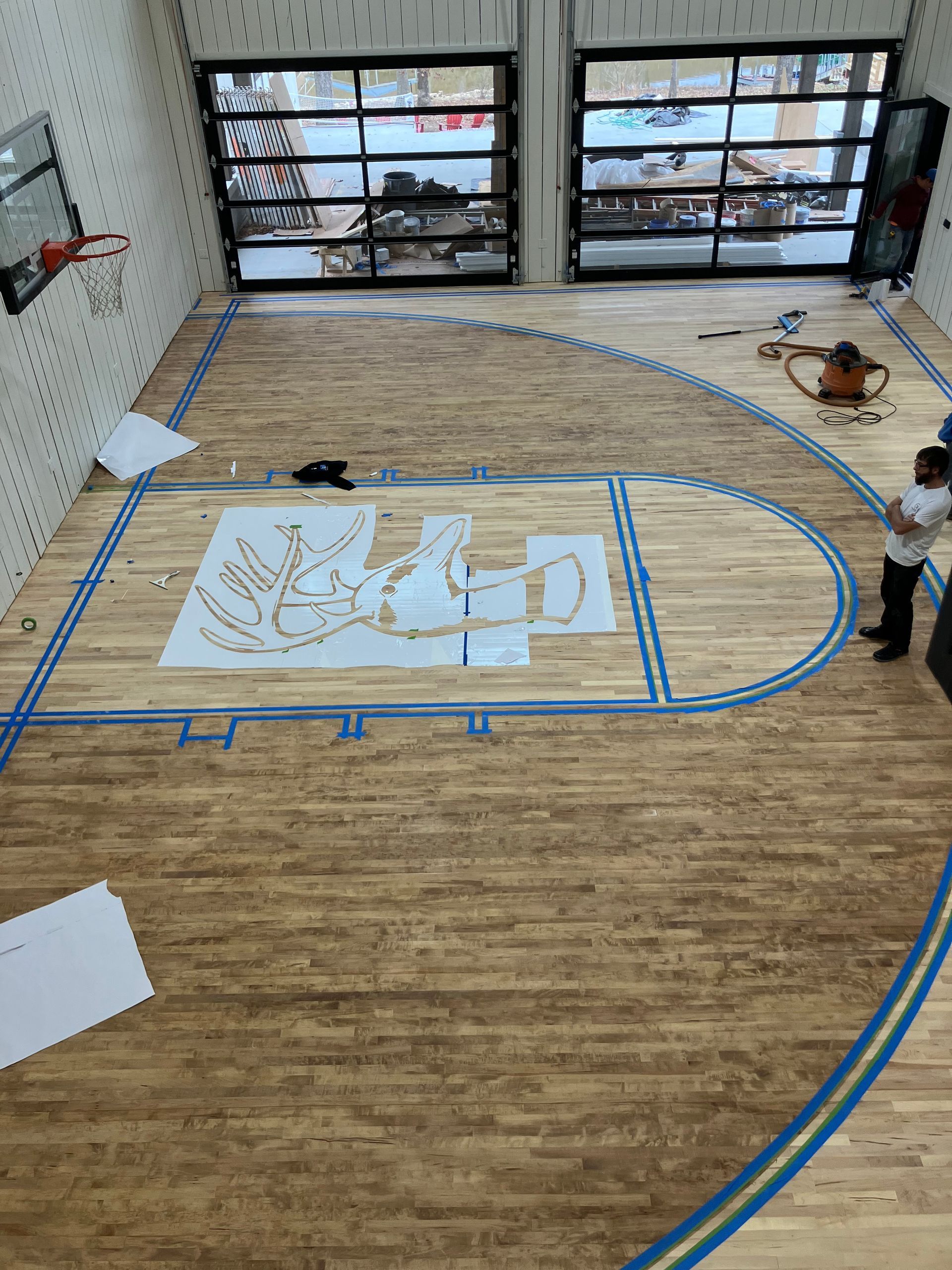 Indoor room with taped floor plan, large windows, and a central white layout drawing on the floor