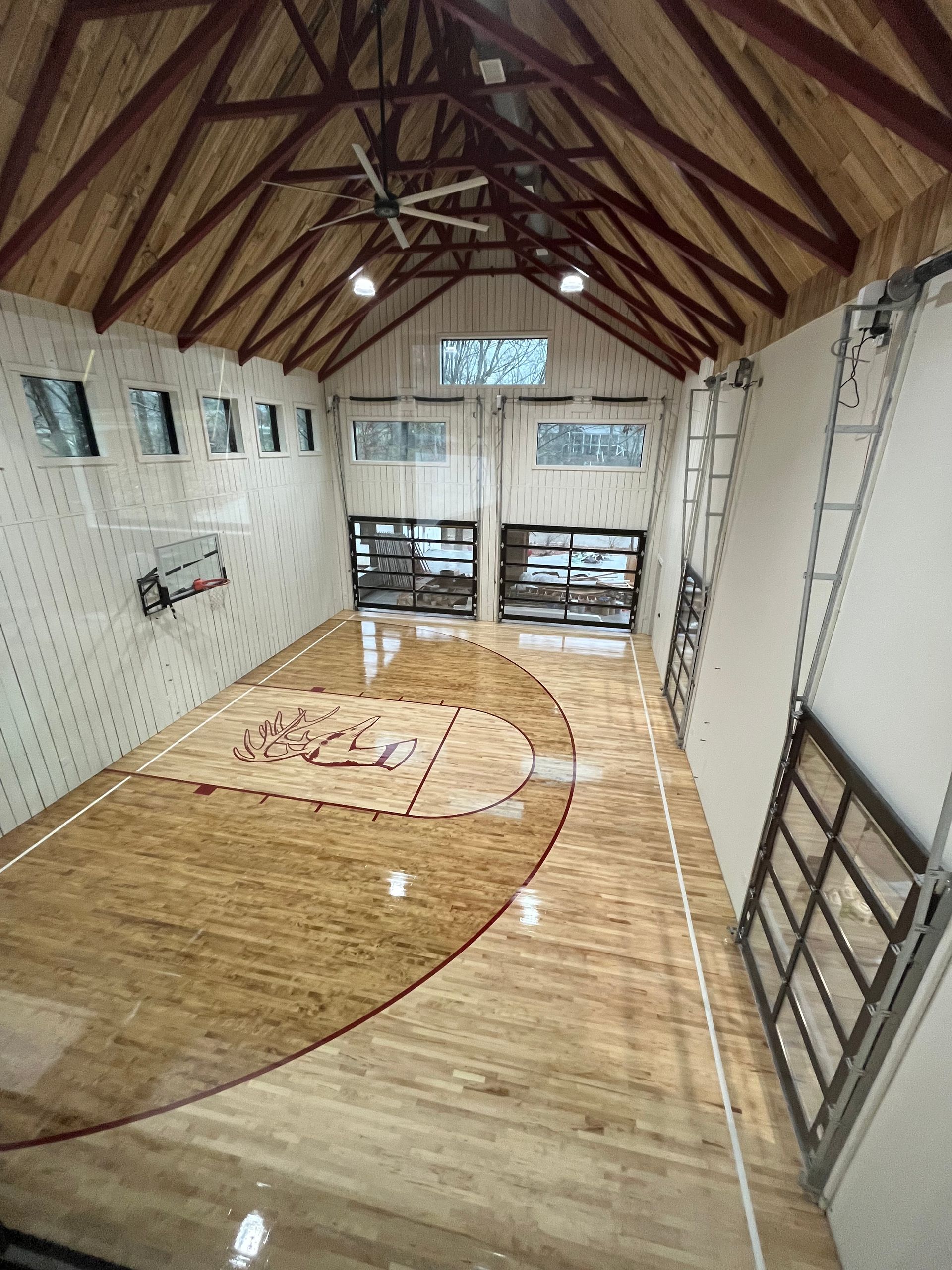 Empty indoor sports court with a wooden floor, hoops, and tall windows under a vaulted ceiling