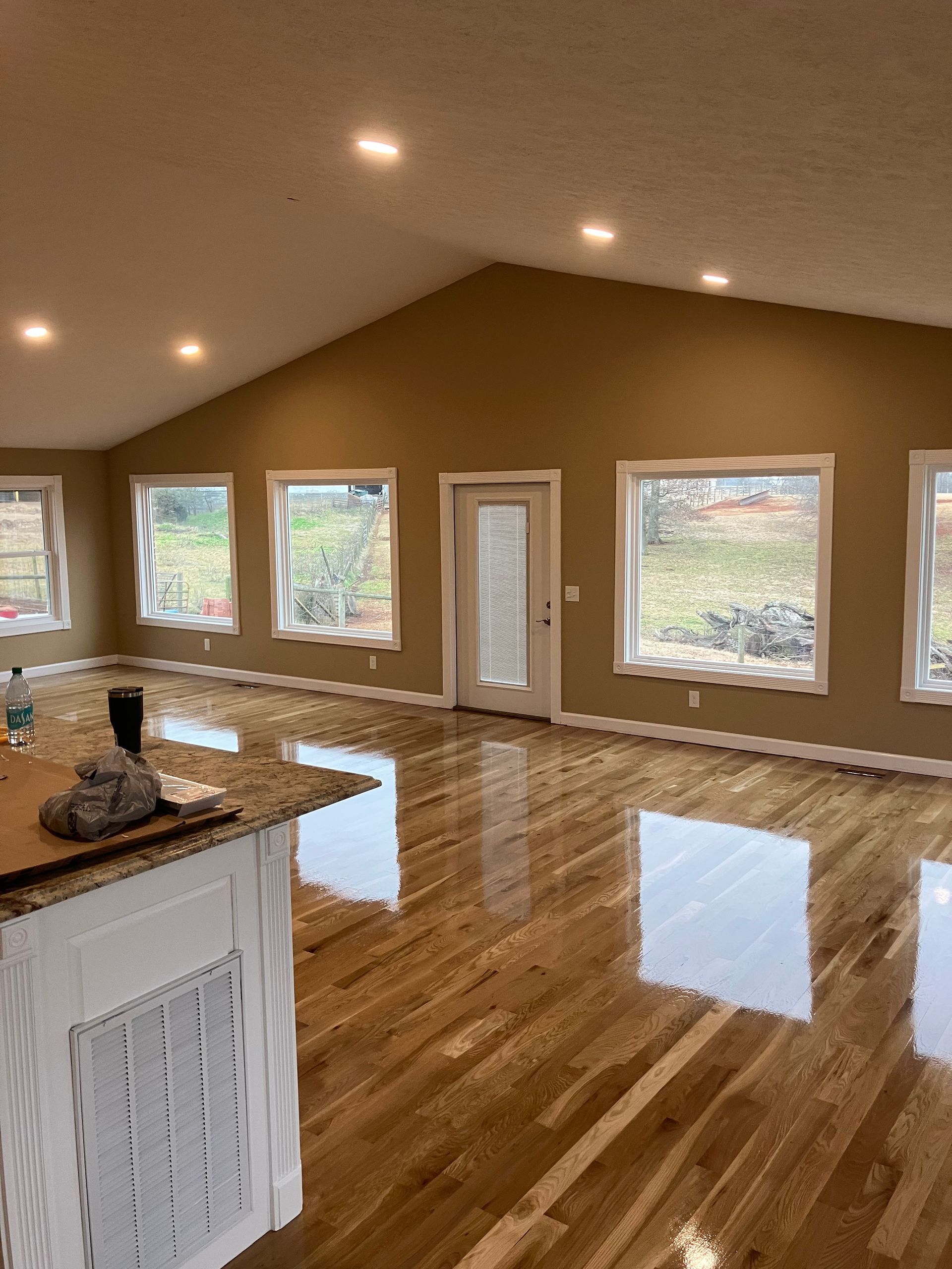 Spacious room with glossy hardwood floors, tan walls, recessed lights, and large windows and glass door.