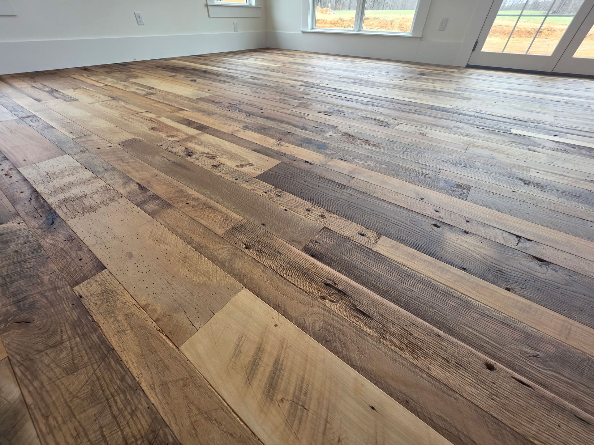 Wide view of rustic wood plank flooring in a bright empty room with large windows.