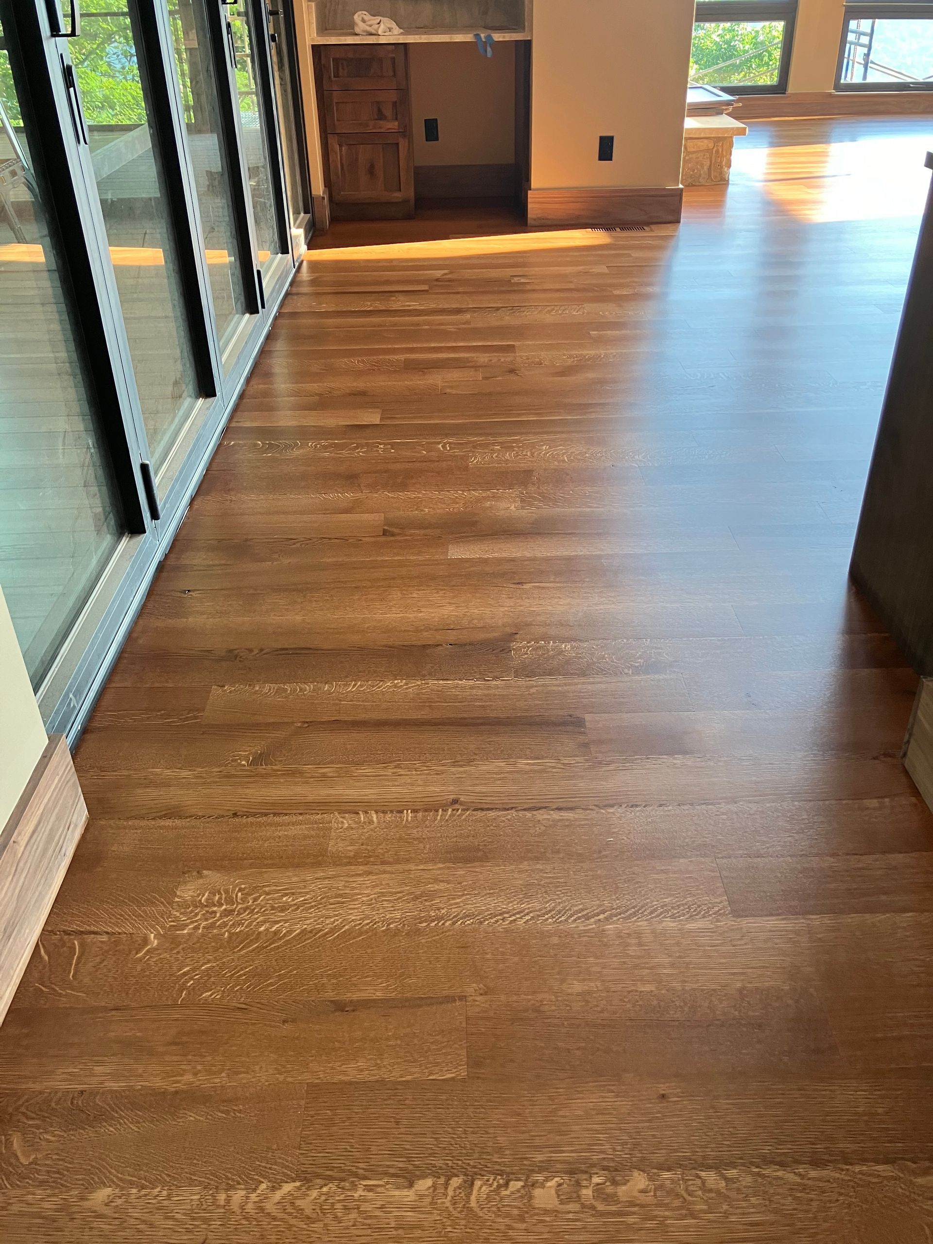 Sunlit hardwood hallway with large windows and a doorway at the end