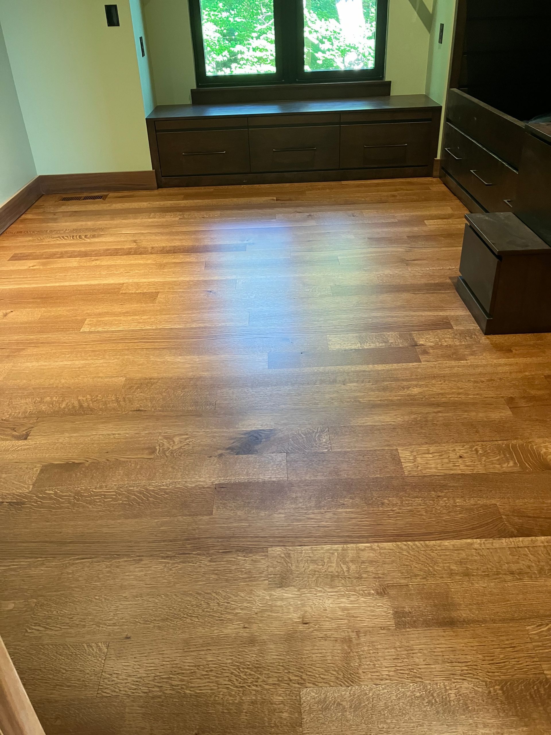Empty room with polished hardwood floors, a window seat, and a dresser by the window.