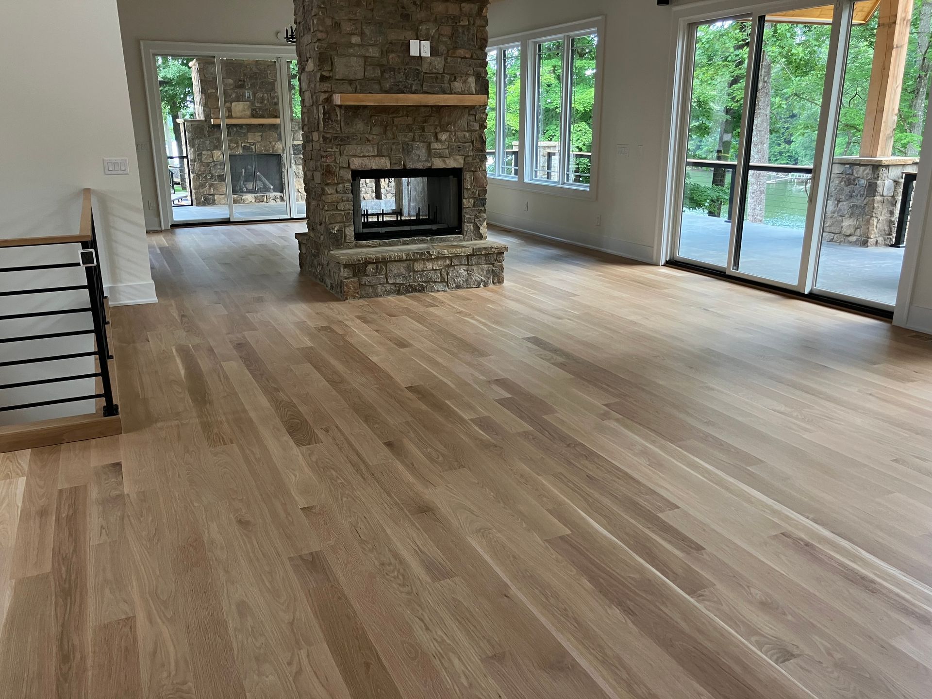 Spacious living room with hardwood floors, stone fireplace, and large windows opening to a deck.