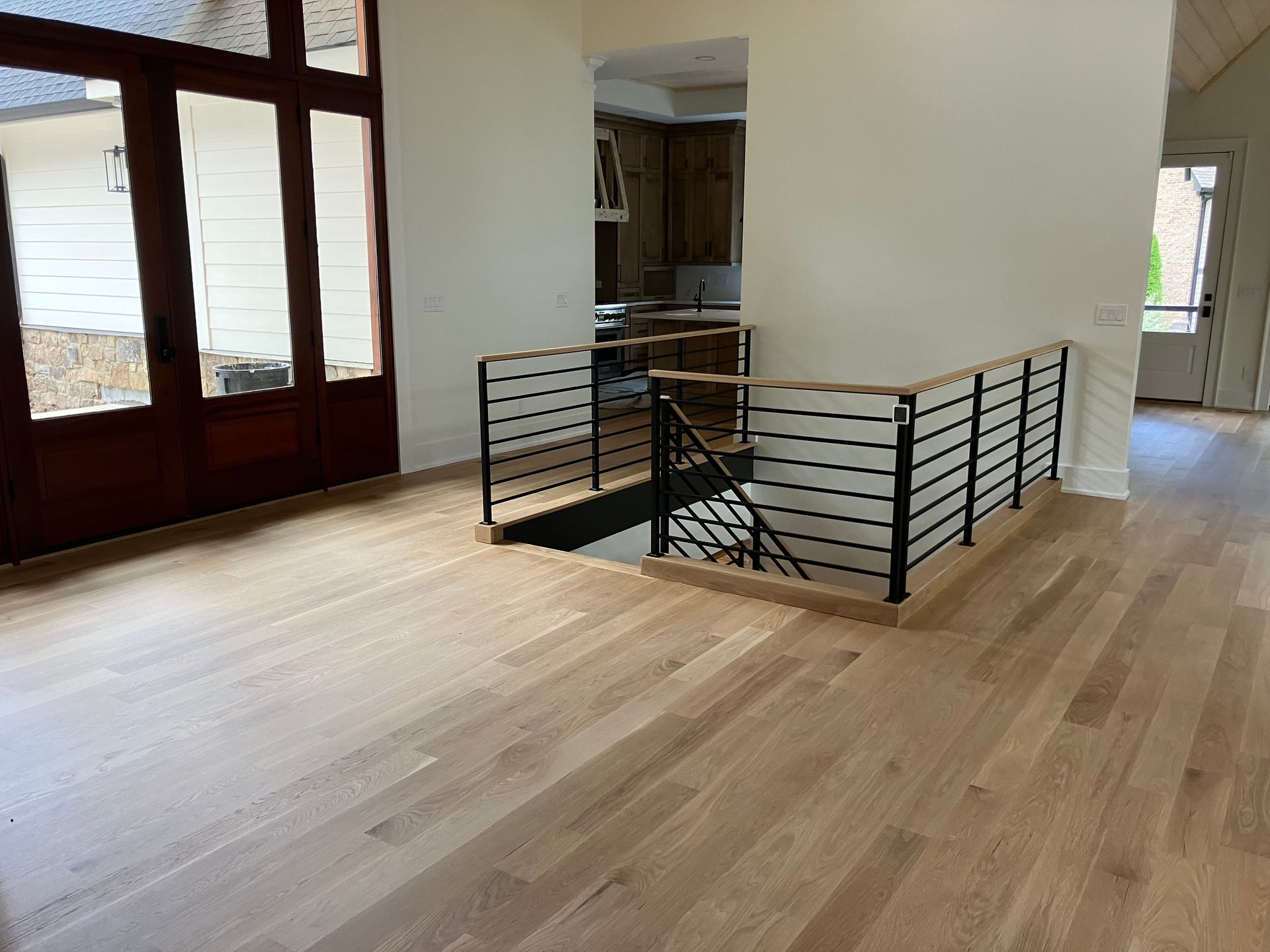 Empty hardwood hallway with stairs opening to a lower level and large windows on the left