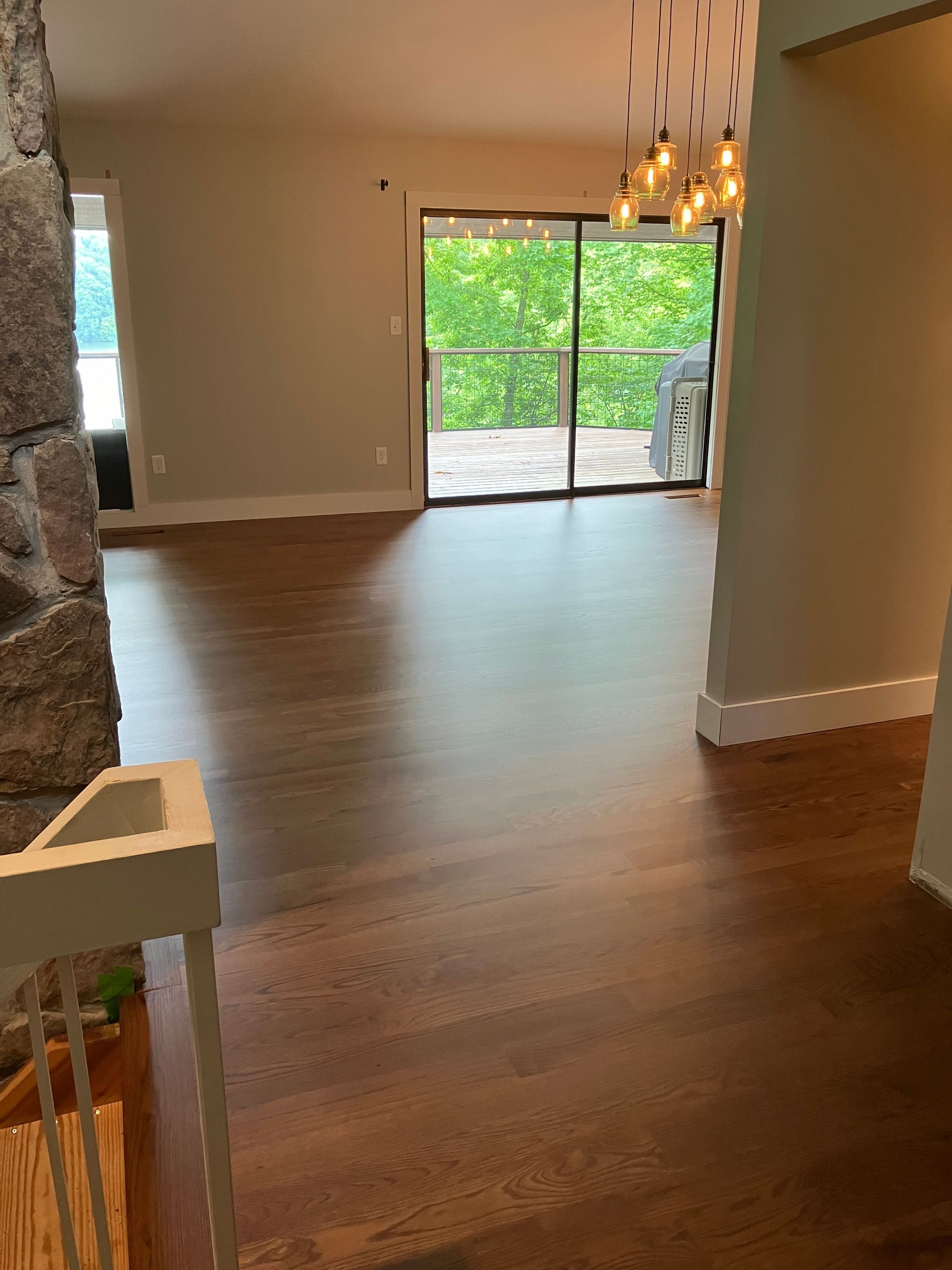 Empty living room with hardwood floors, stone fireplace, chandelier, and sliding glass doors to a green patio.