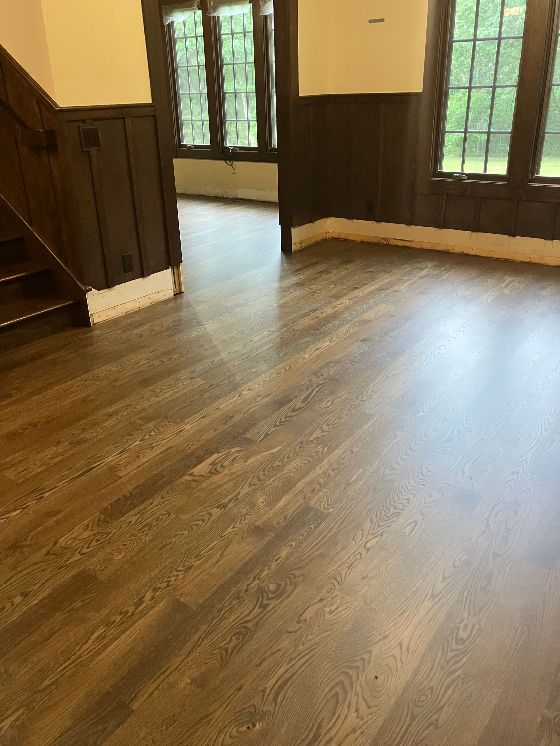 Empty room with wood floors, dark paneled walls, and tall windows letting in daylight