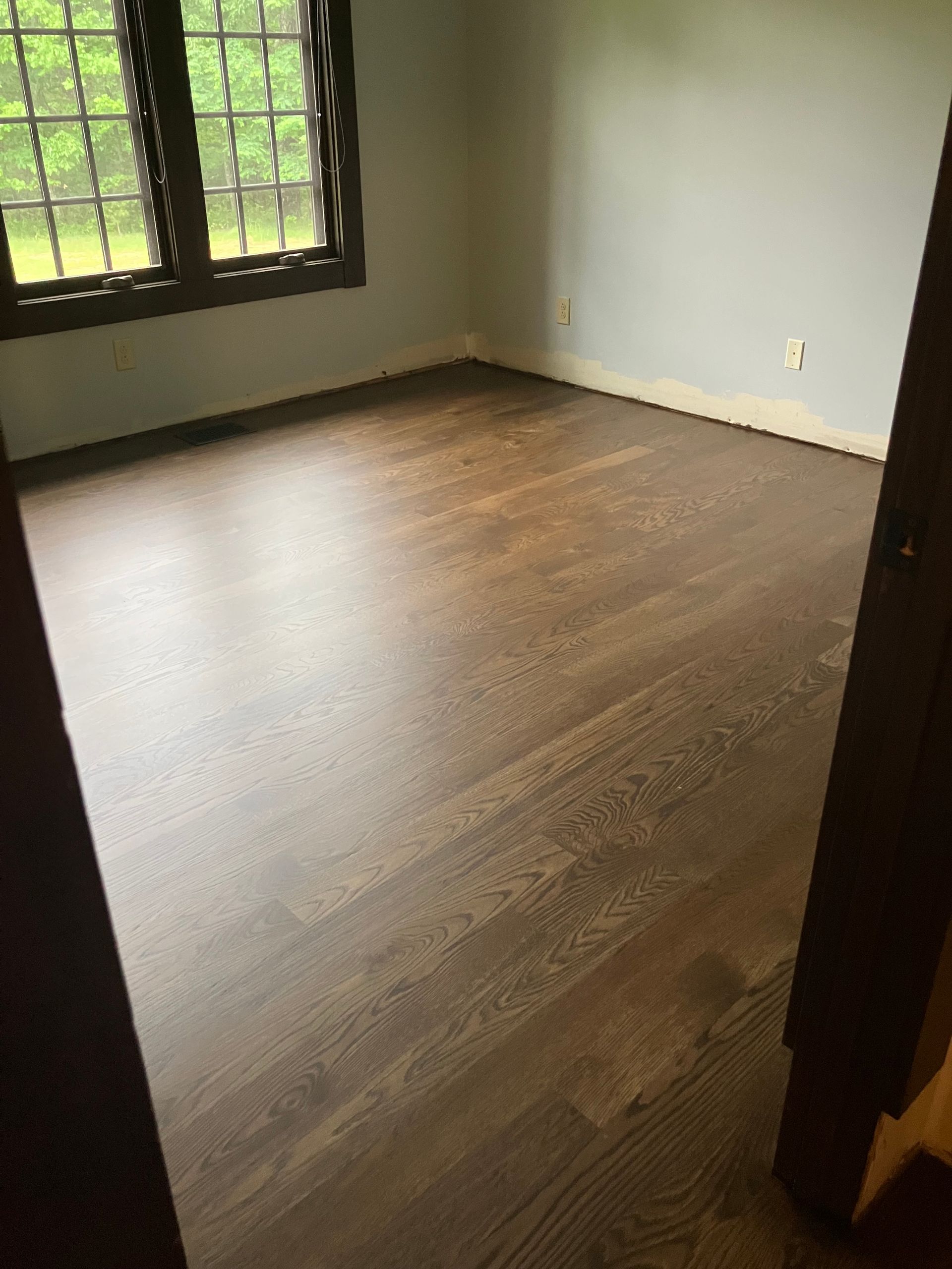 Empty room with dark wood floors, white walls, and a window letting in daylight