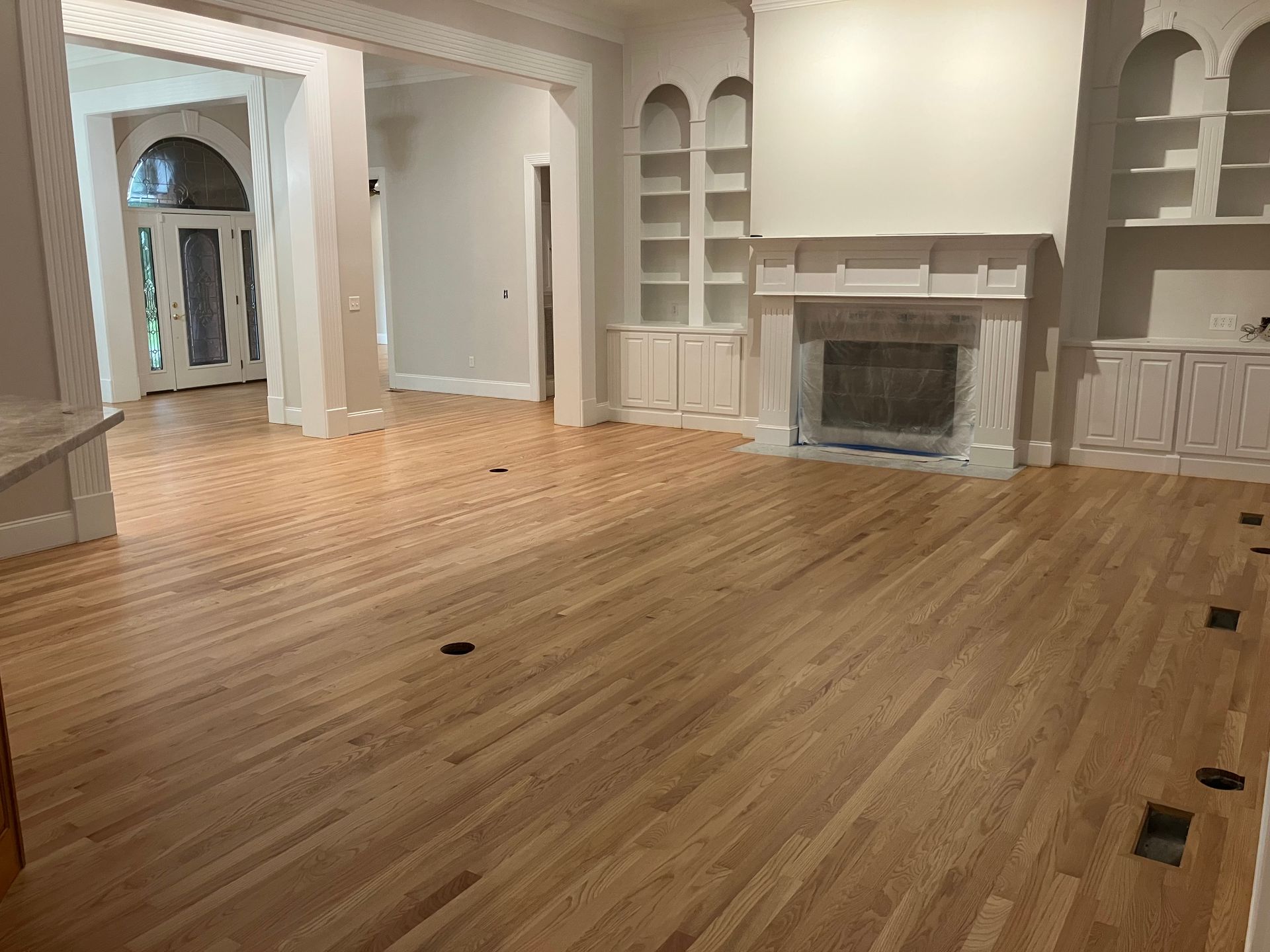 Empty living room with hardwood floors, white built-ins, and a fireplace.