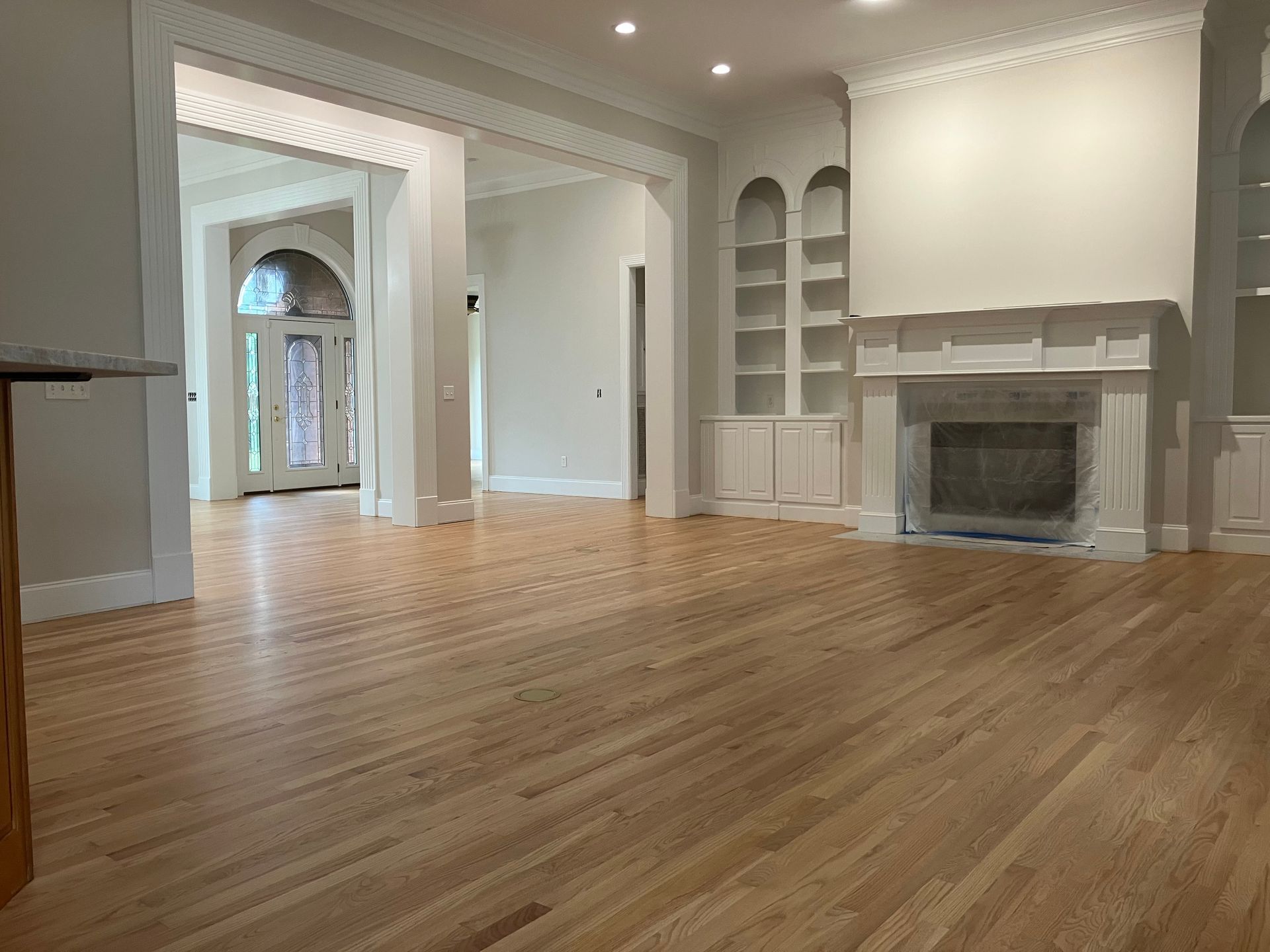 Spacious empty living room with hardwood floors, white walls, arched doorway, and a fireplace.