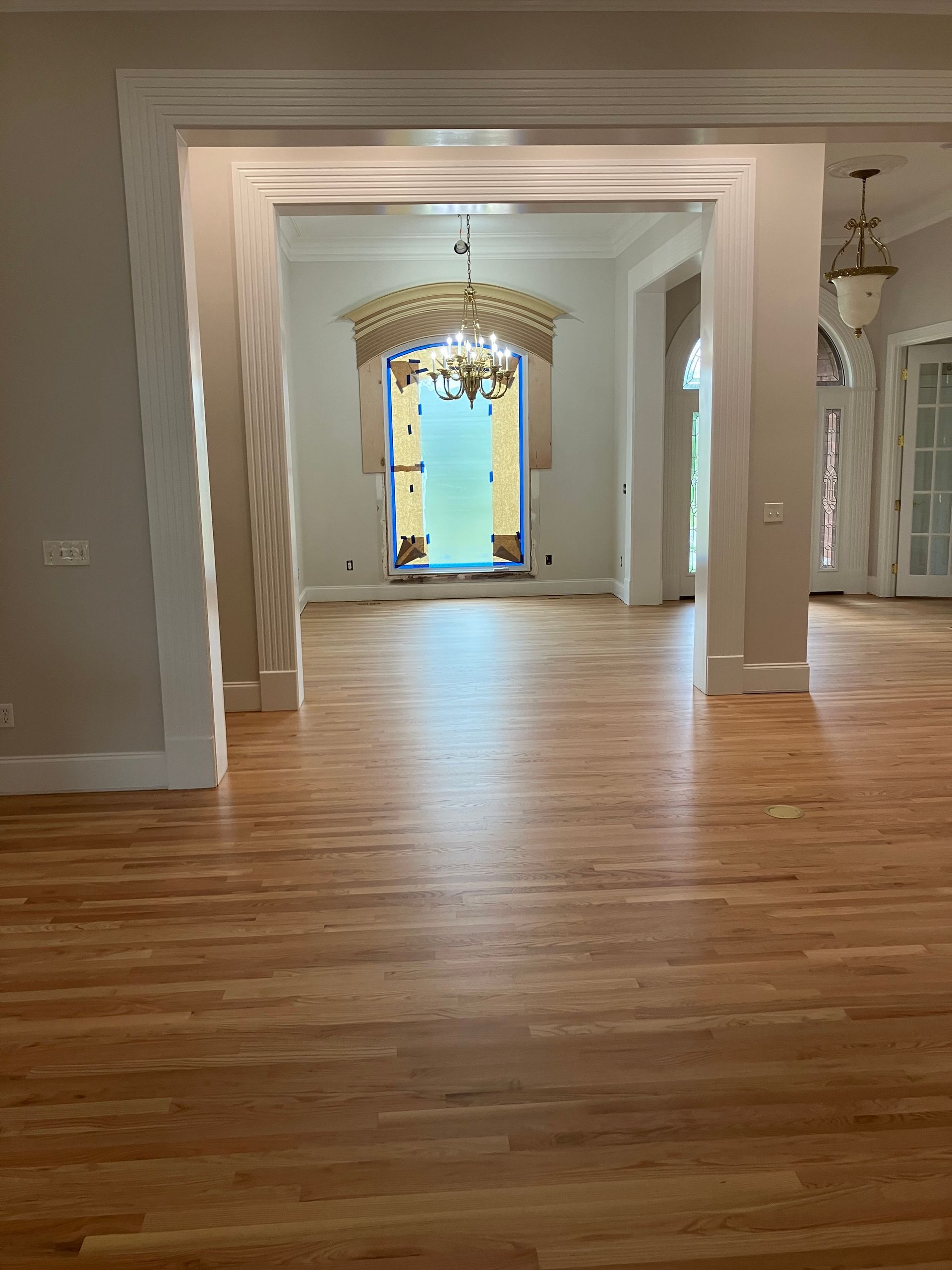 Empty elegant room with hardwood floors, ornate trim, and a bright blue doorway in the back.