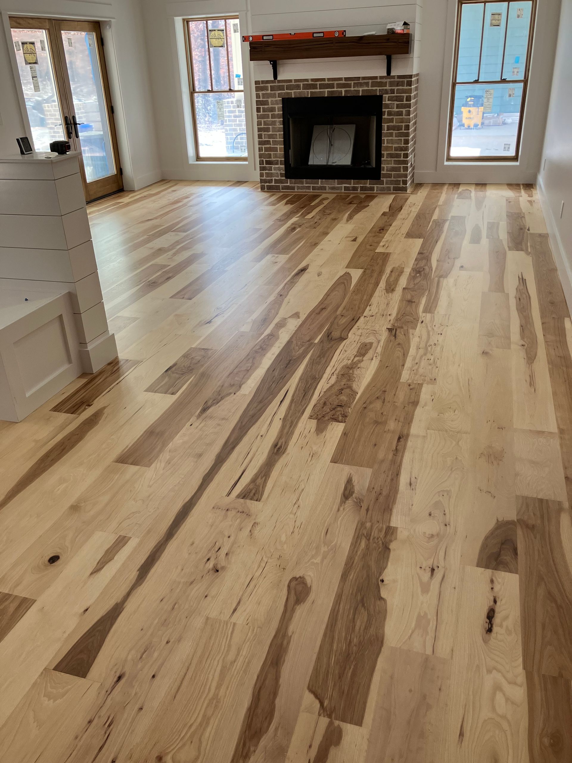 Empty living room with light wood floors, white walls, and a fireplace between two windows.
