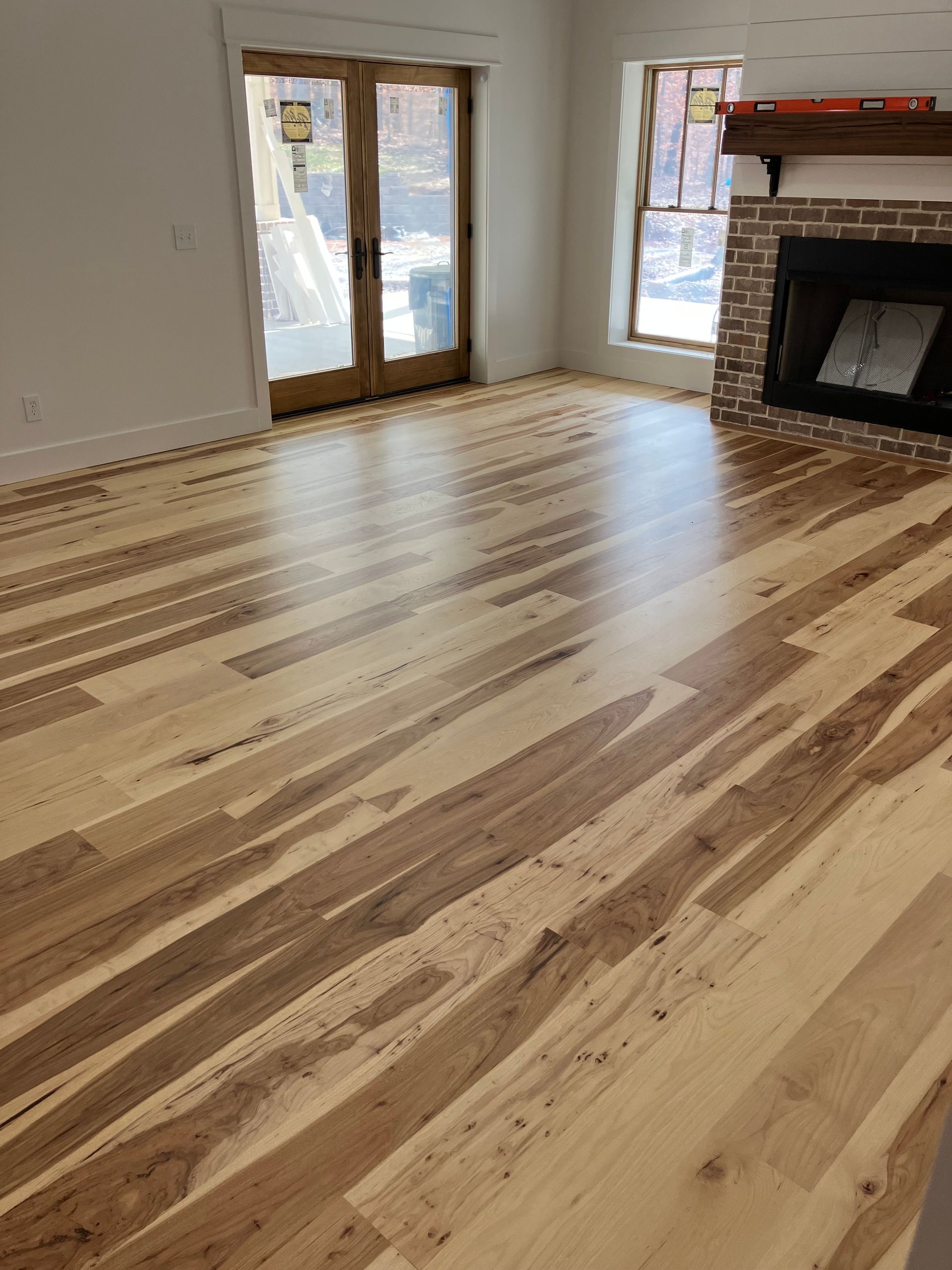 Empty living room with light wood floors, French doors, and a fireplace.