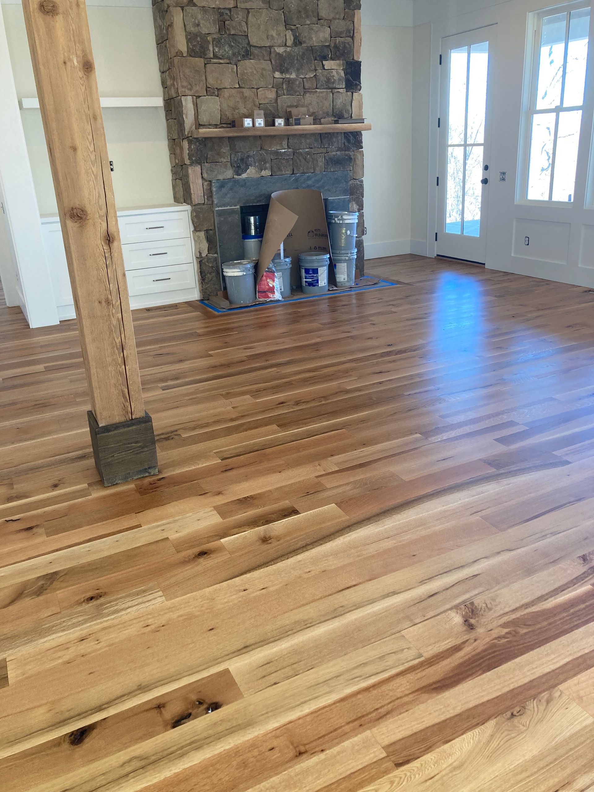 Empty room with wood floors, stone fireplace, and French doors letting in light.