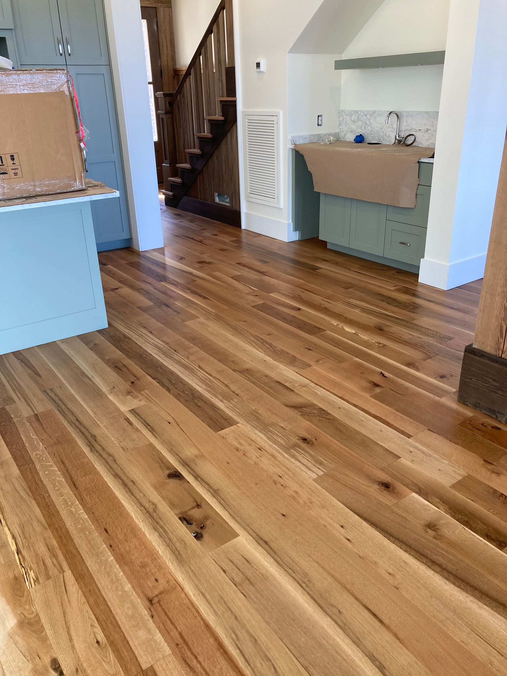 Sunlit hardwood floor in a modern home interior with stairs and a small sink area