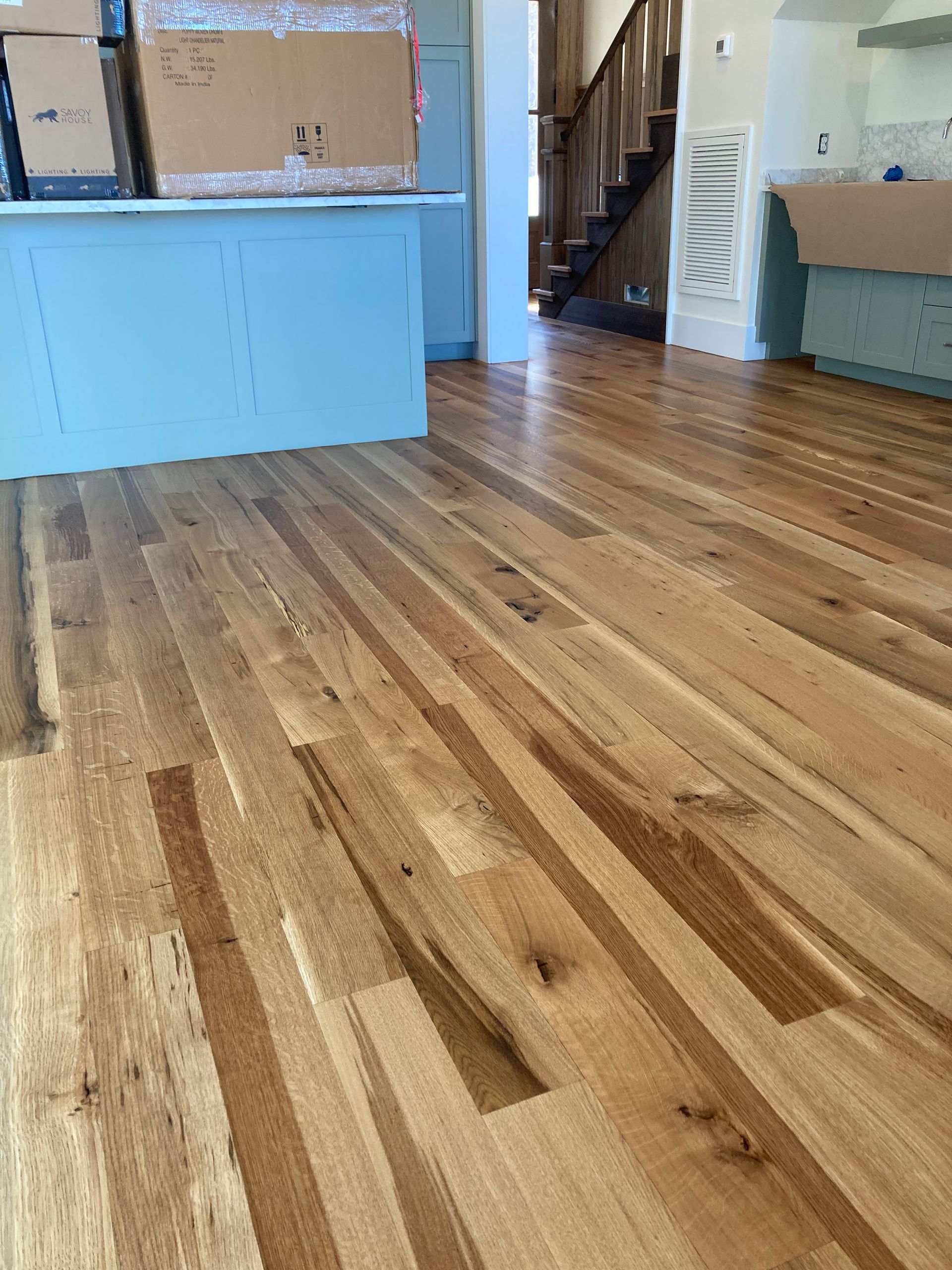 Empty room with polished wood floor, light blue cabinets, and a staircase in the background