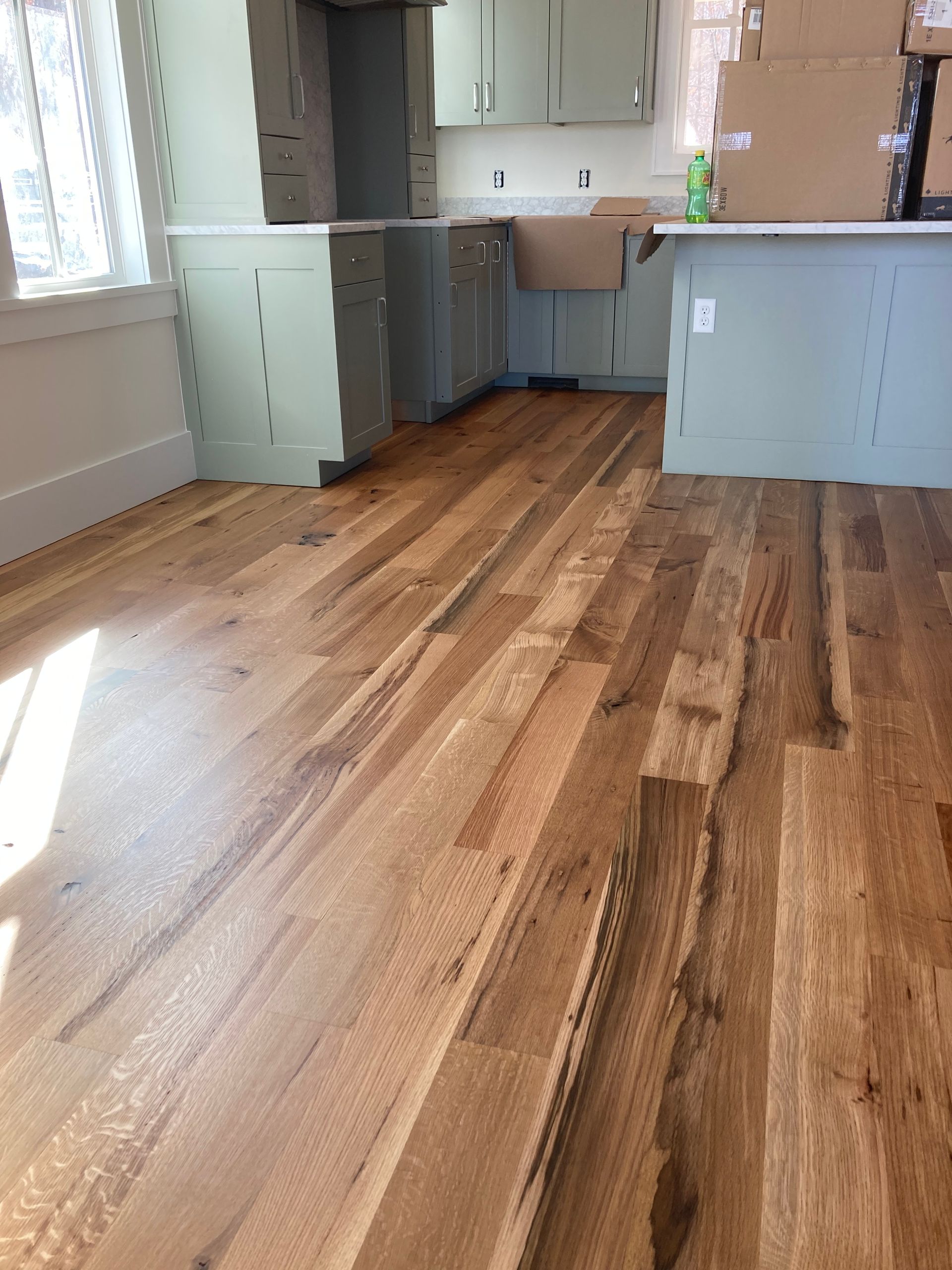 Empty room with wood floors, light green cabinets, and a window by the sink area
