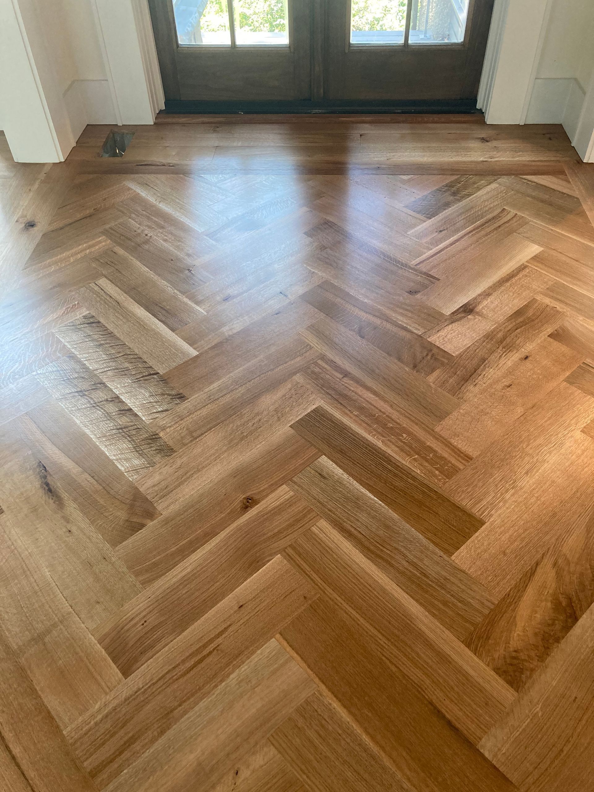 Herringbone wood floor in a sunlit entryway with double doors and windows.