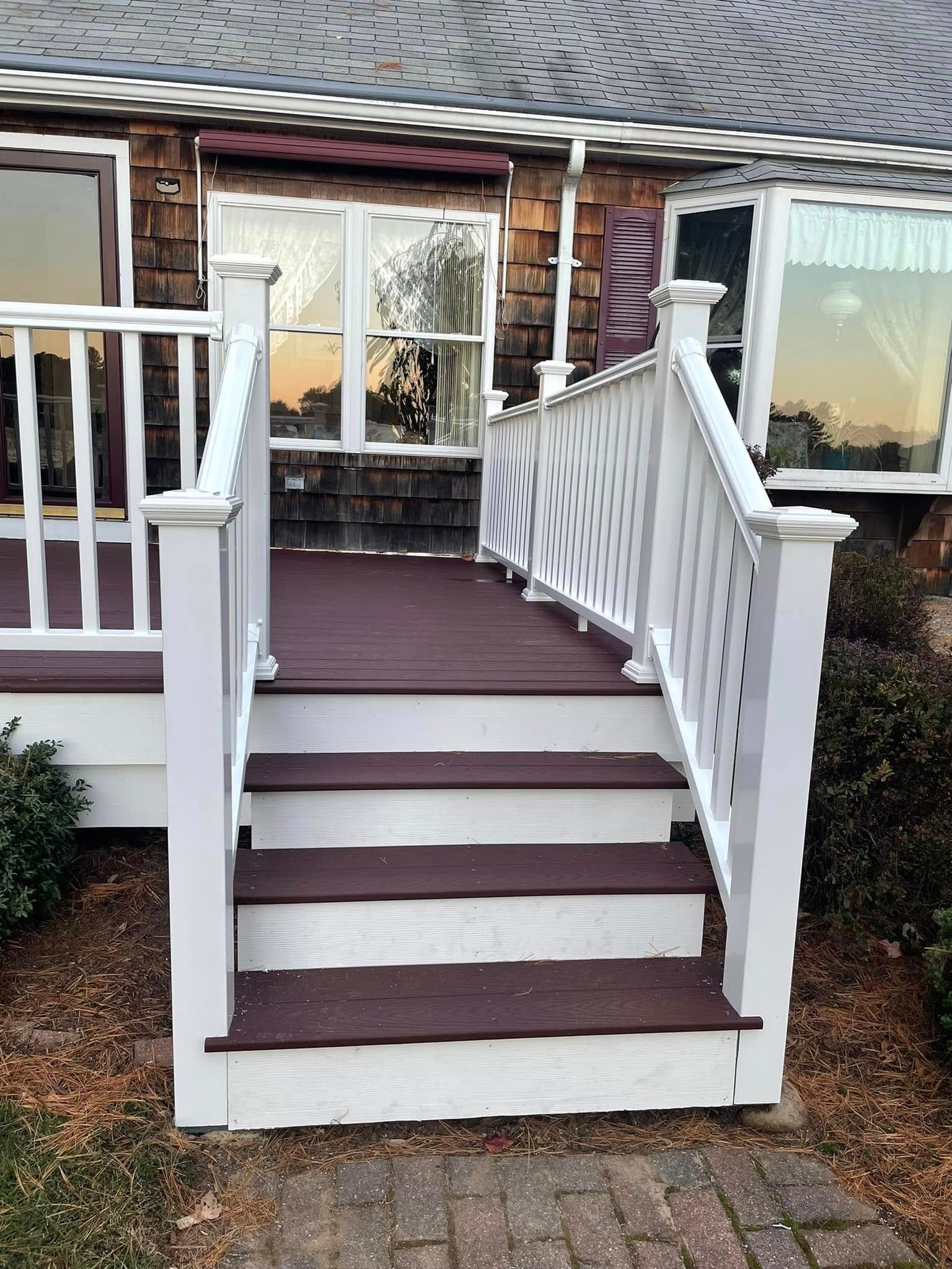 Front porch steps with white railings and brown treads leading to a house entrance.