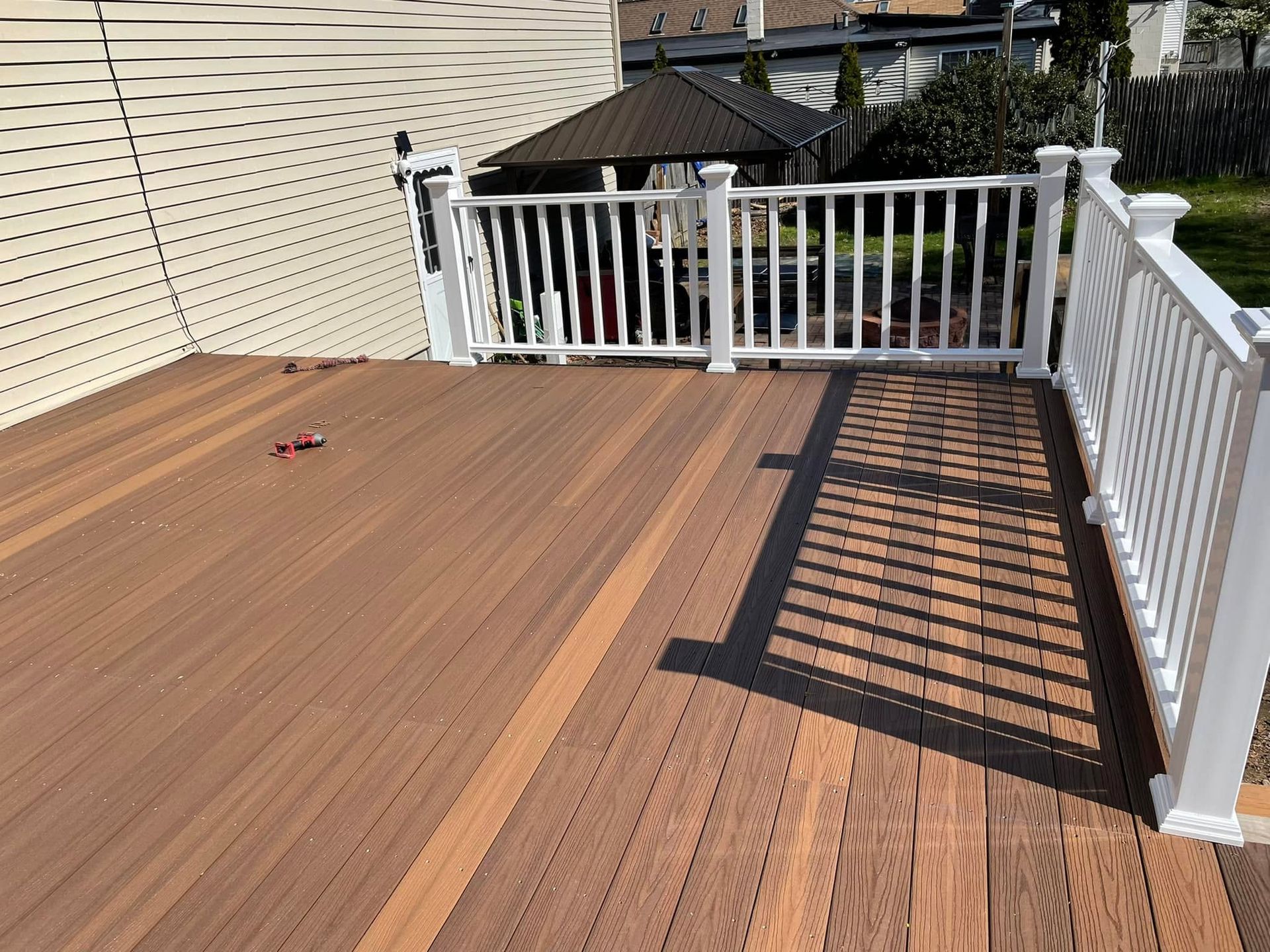 Wooden deck with white railing and pergola shadows in a backyard.