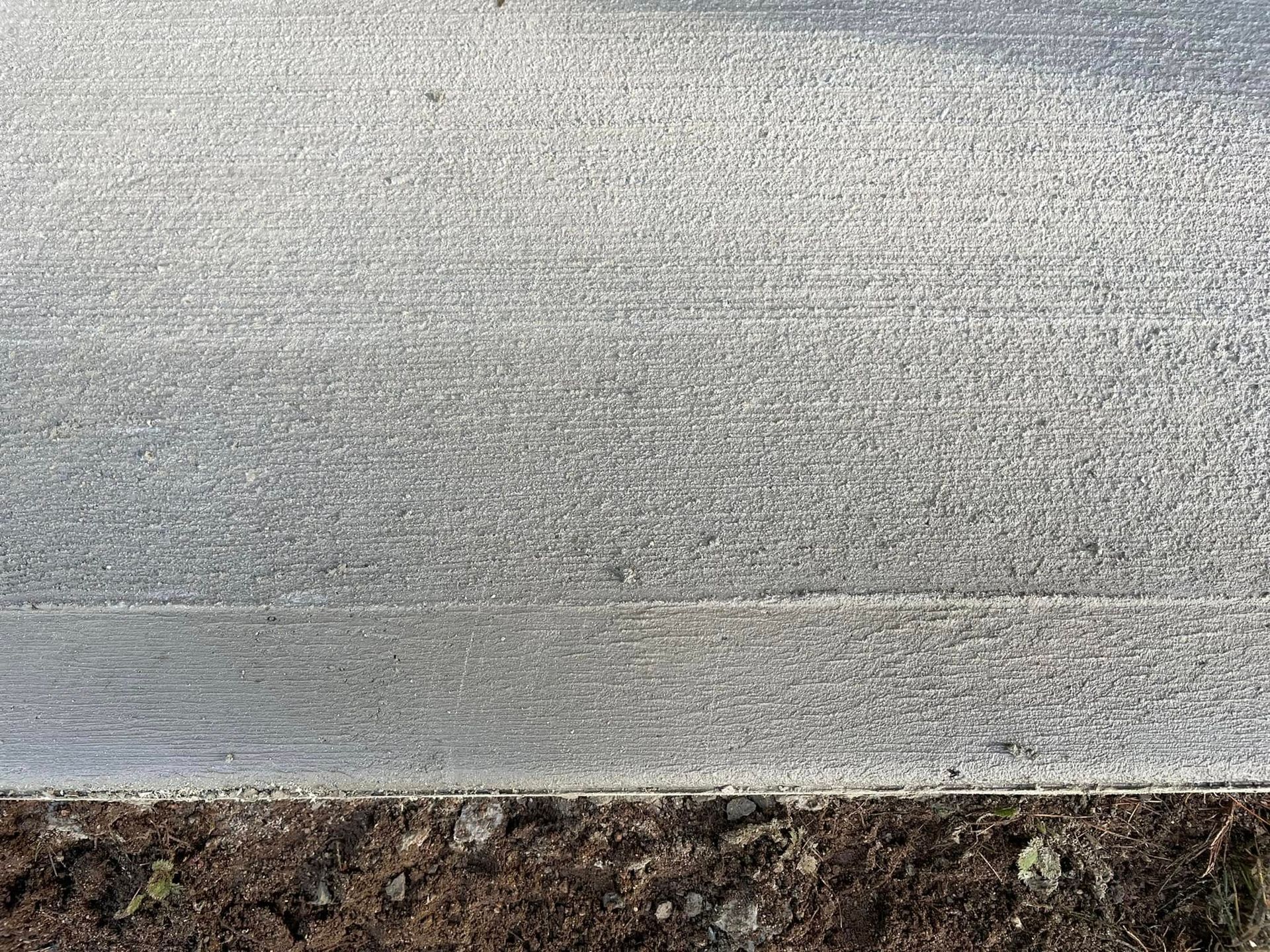 Gray textured wall with a strip of brown dirt or mulch along the bottom edge