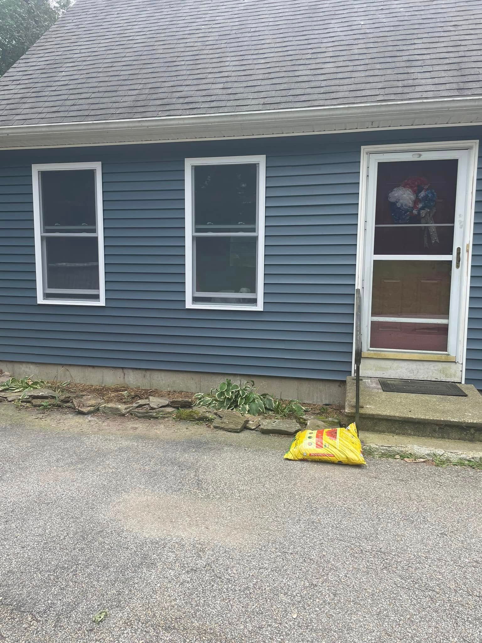 Blue house exterior with two windows, a screen door, and a yellow caution sign on the driveway