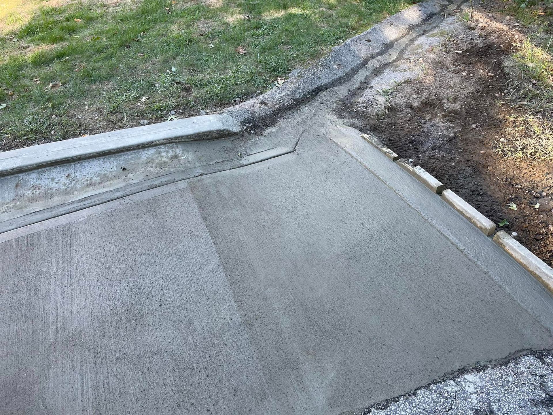 Concrete sidewalk corner with a raised curb and patchy grass beside it