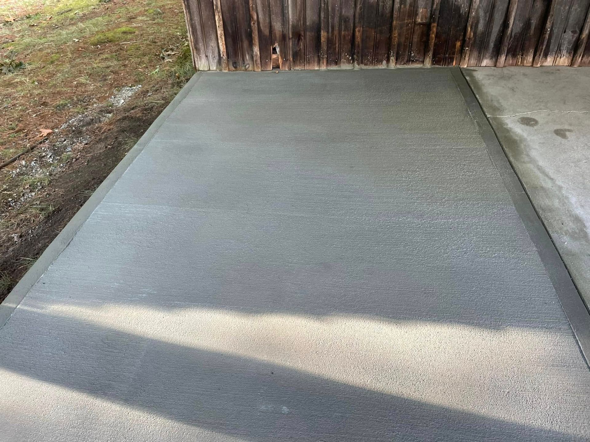 Concrete driveway leading to a wooden fence with a shadow across it