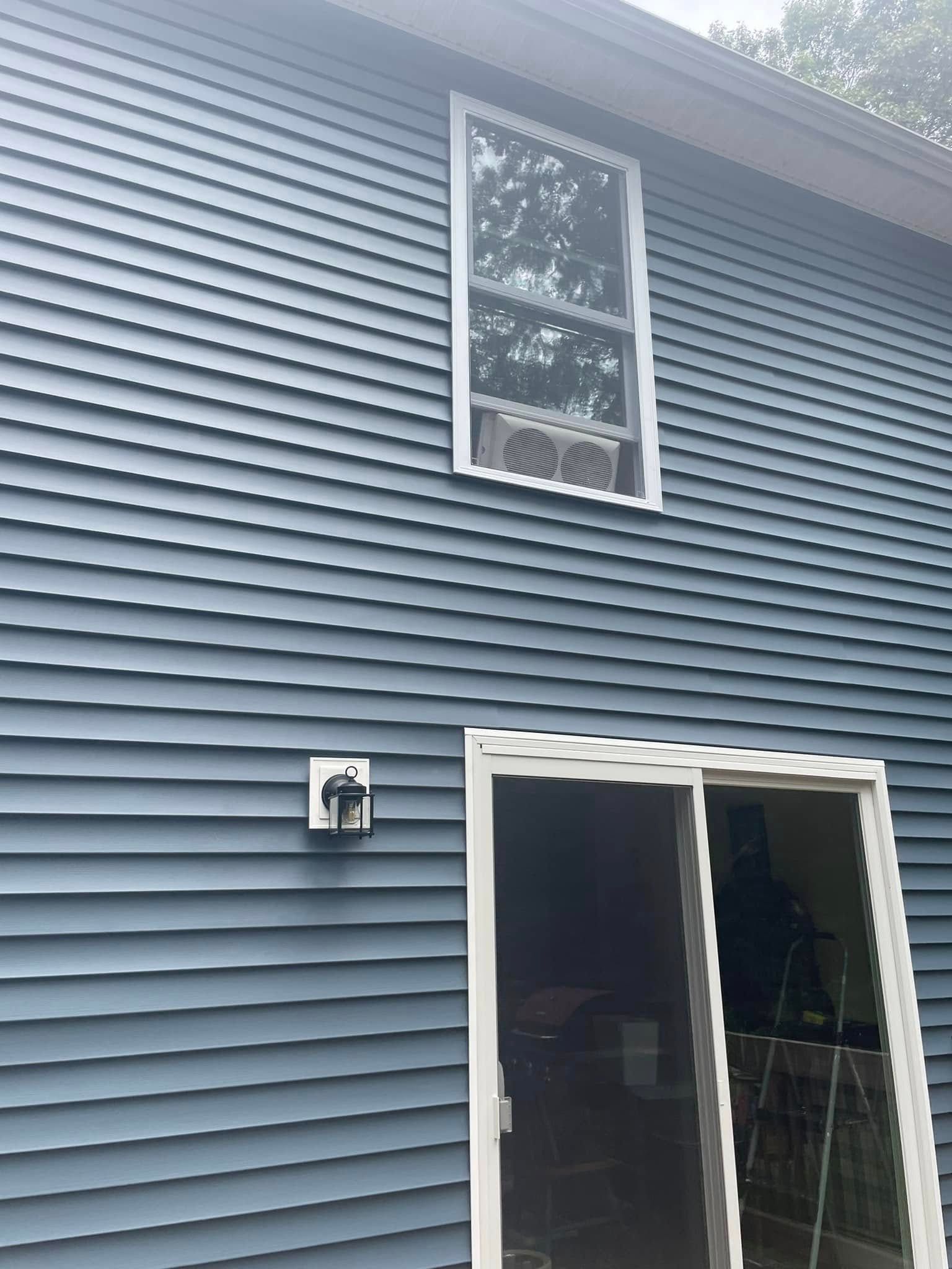Blue vinyl house exterior with white-trimmed window and sliding glass door under a small light fixture
