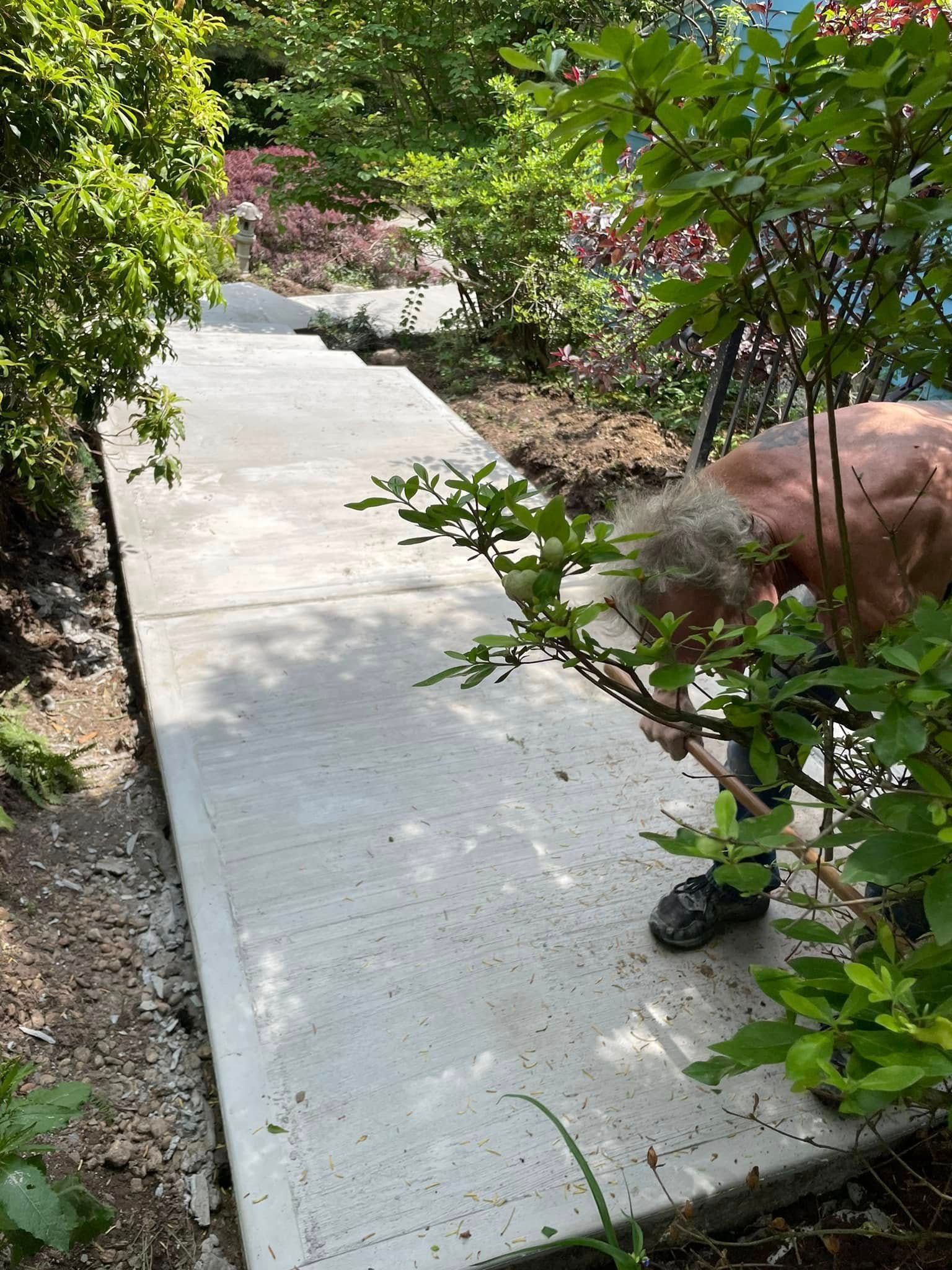 Fresh concrete walkway bordered by shrubs and flowers in a garden, with a person crouching at the right edge