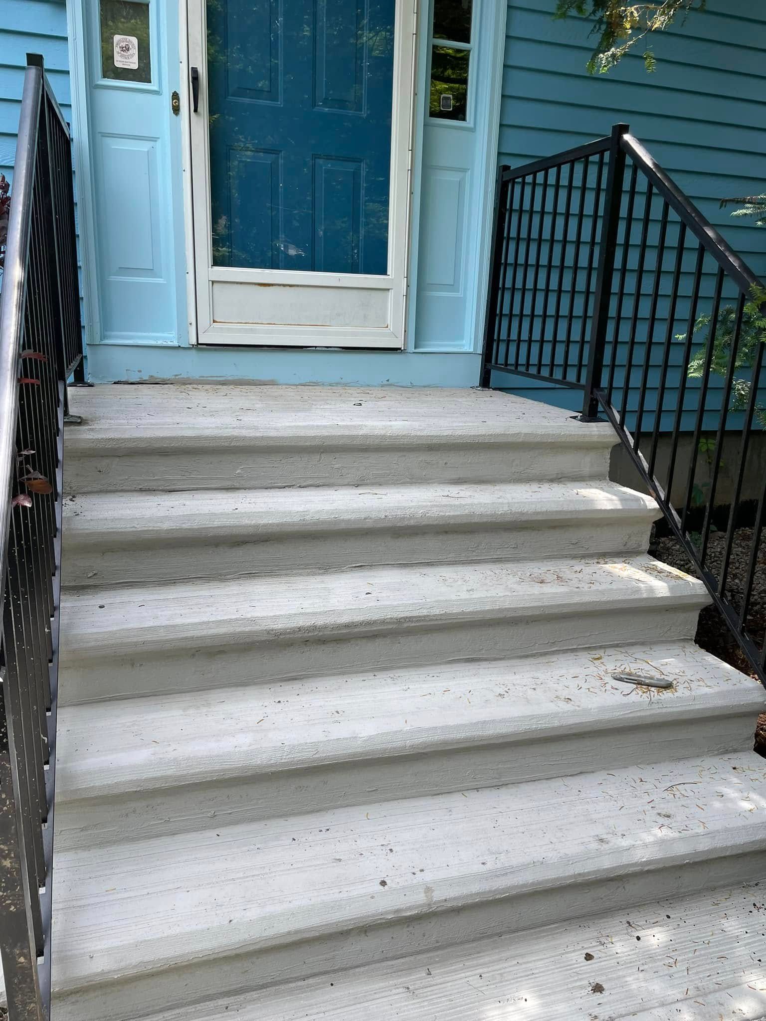 Concrete front steps leading to a blue front door with black railings on both sides