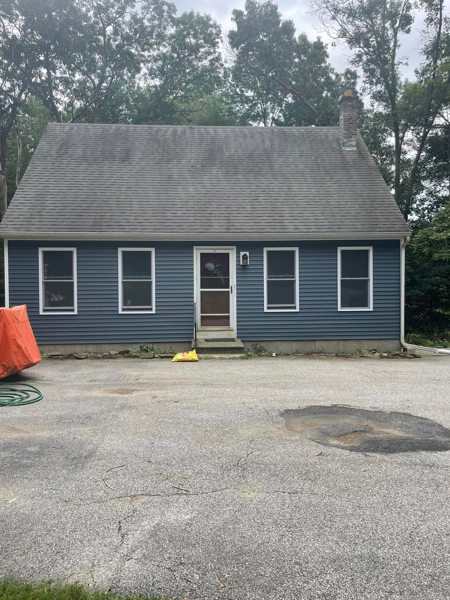 Small dark-blue house with a steep shingled roof and gravel driveway, seen from the front.