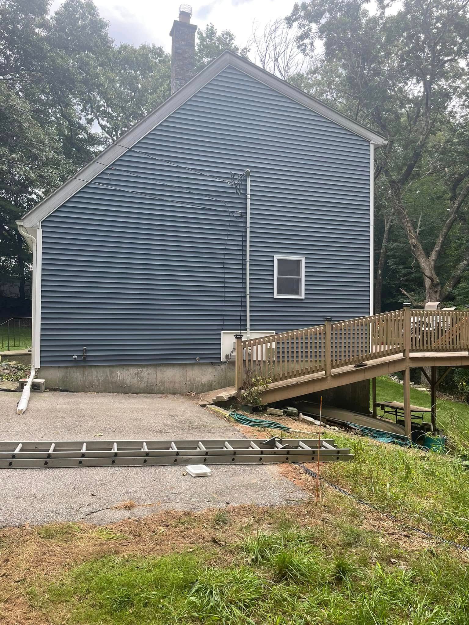 Gray house with steep roof, small window, and wooden ramp in a wooded yard