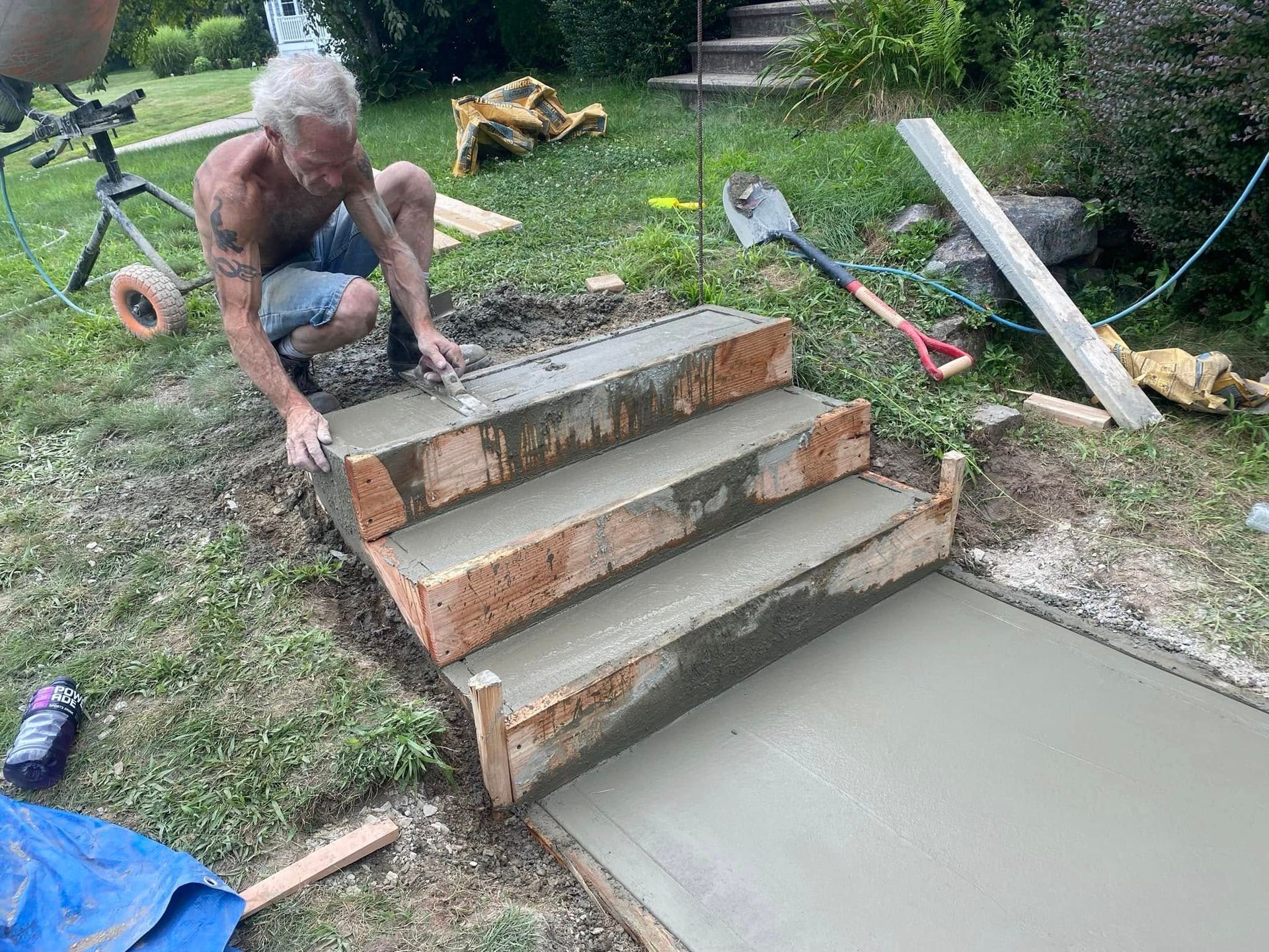 Person smoothing wet concrete steps beside a freshly poured slab in a grassy yard
