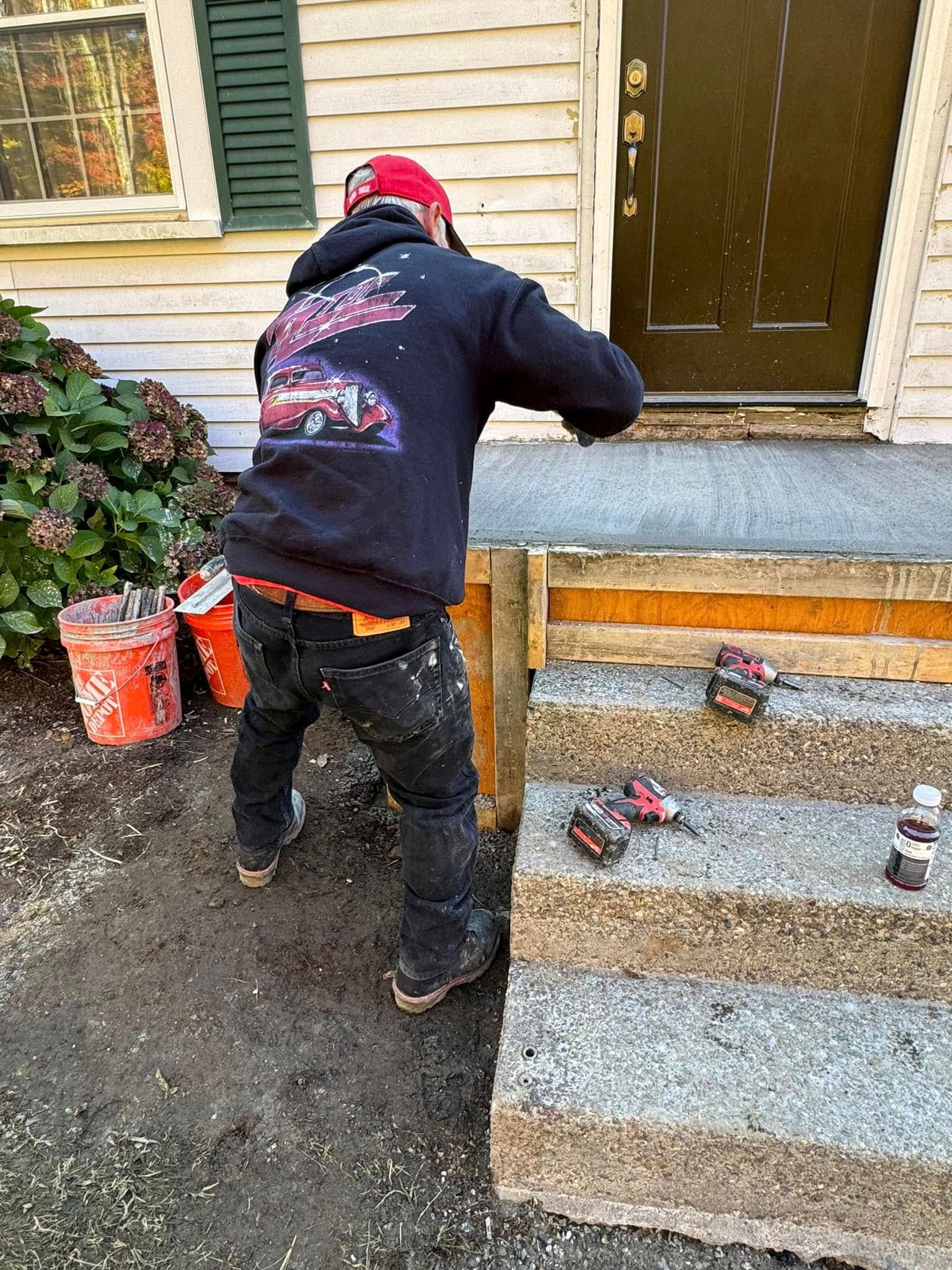 Worker in black hoodie and red beanie painting a front porch steps and doorway.