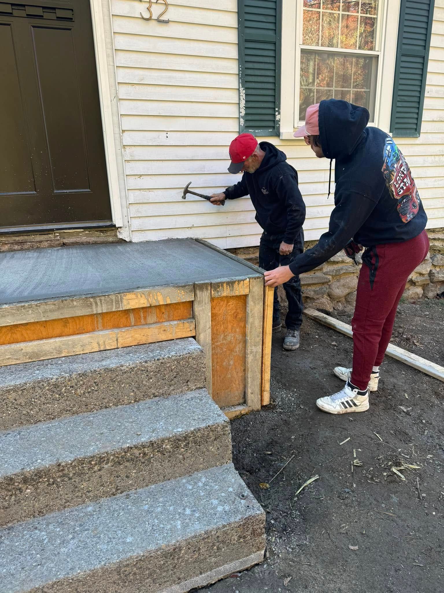 Two people painting a house’s front steps and porch with rollers and brushes.