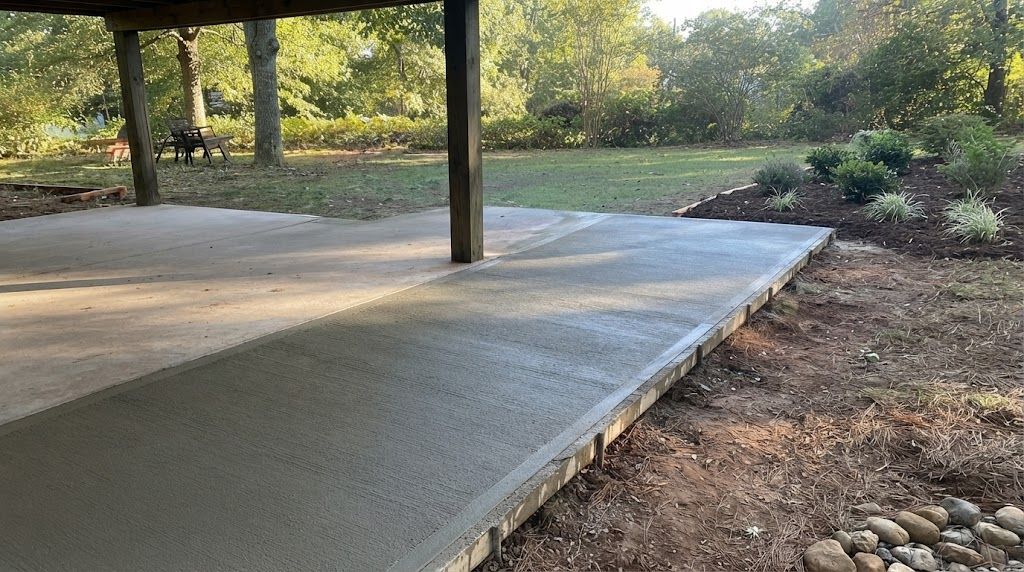 Concrete patio slab with a support post beside a landscaped yard and trees