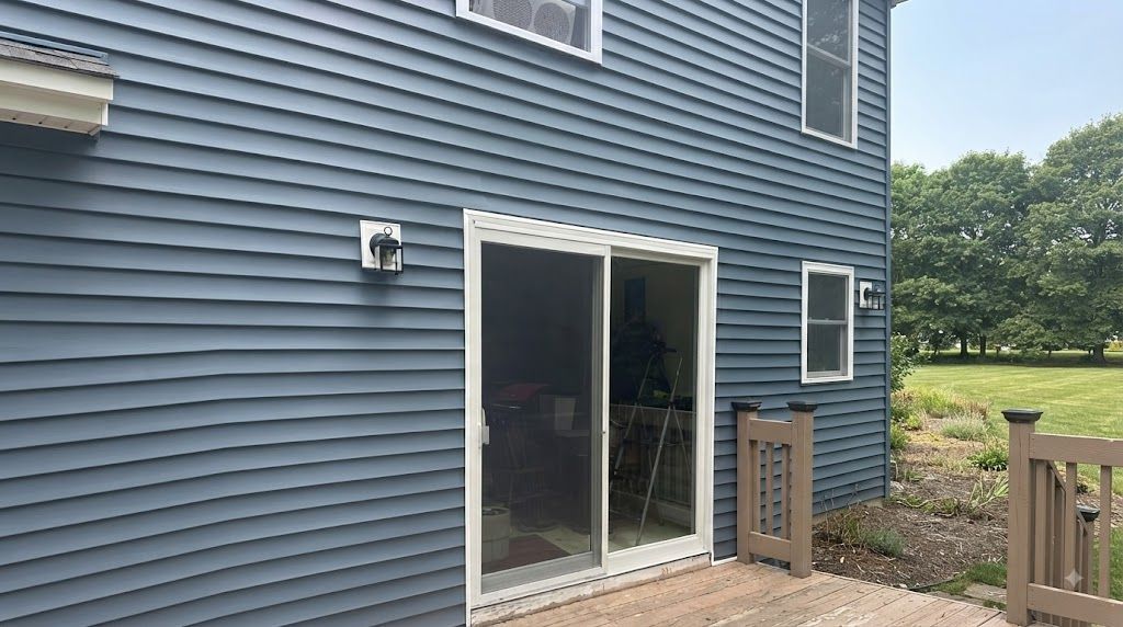 Blue house exterior with sliding glass door and small wooden deck leading to a grassy yard