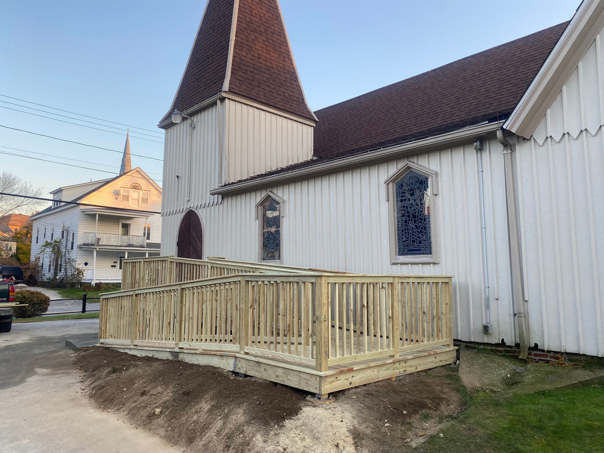 Small wooden deck under construction beside a white church with a steep brown roof.