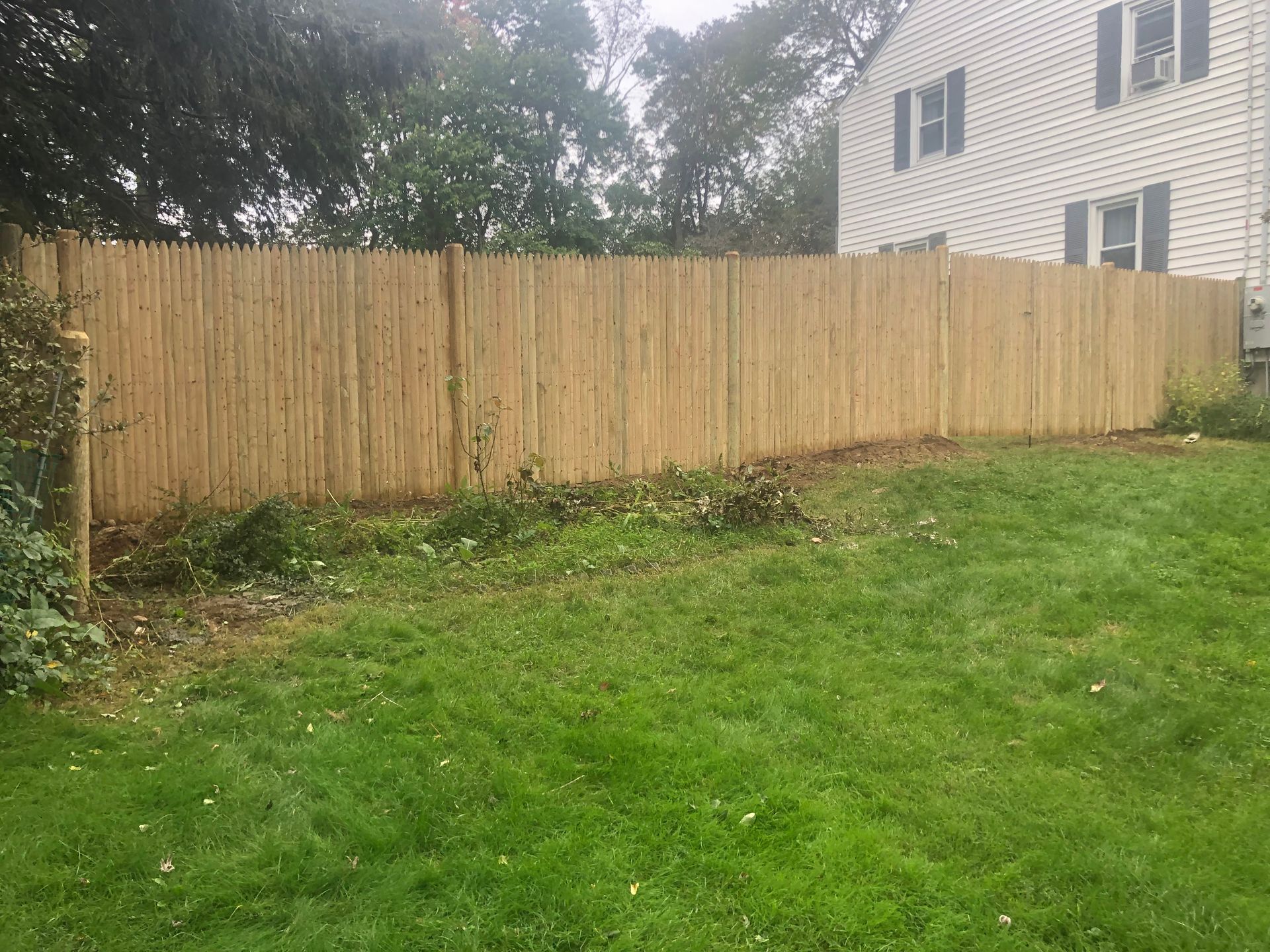 Backyard with green grass and a wooden privacy fence beside a white house