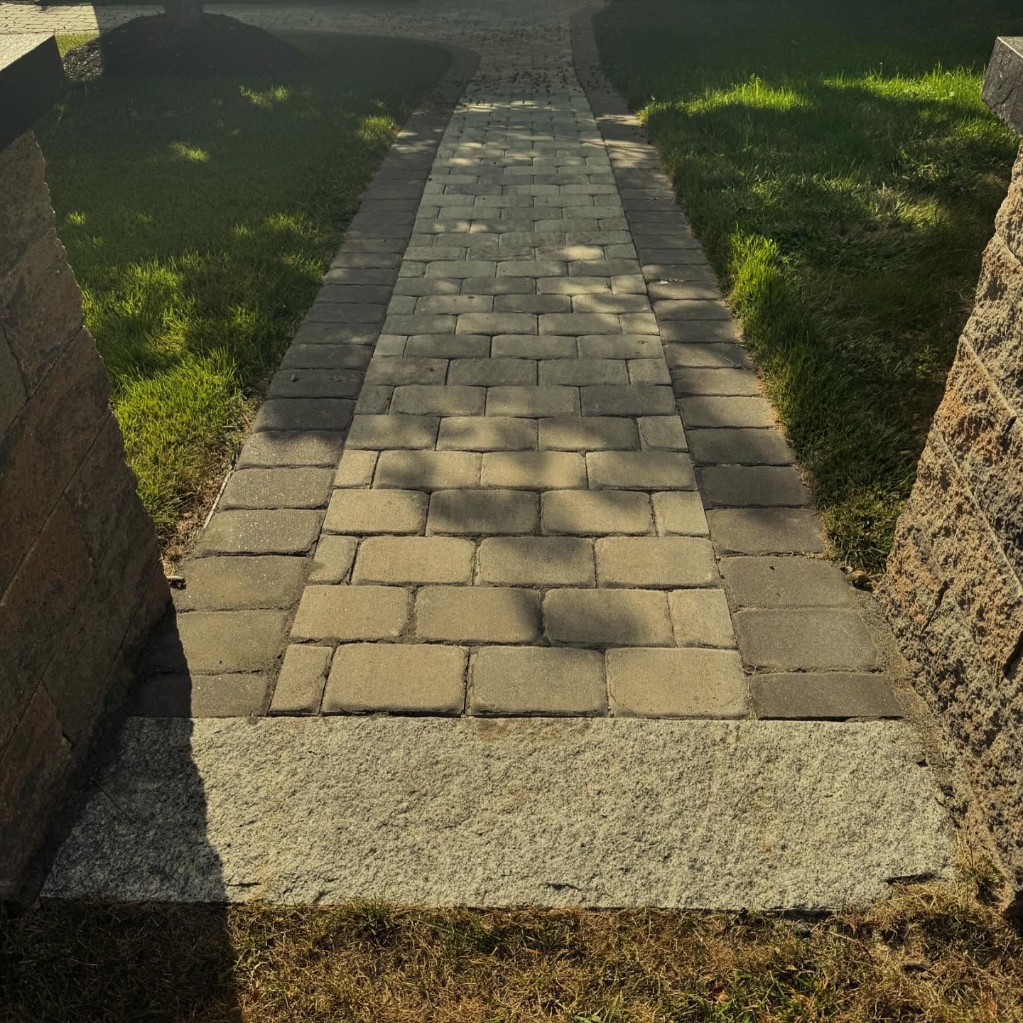 Brick walkway leading through a sunny grassy yard between stone posts