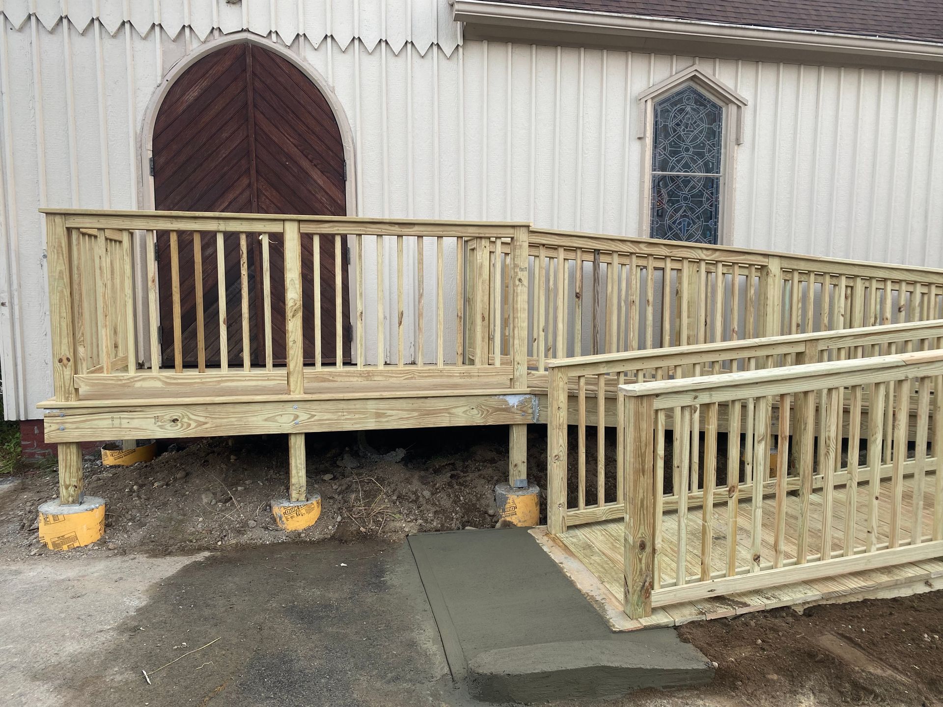 Wooden accessibility ramps and railings beside a beige building, supported by yellow footings.