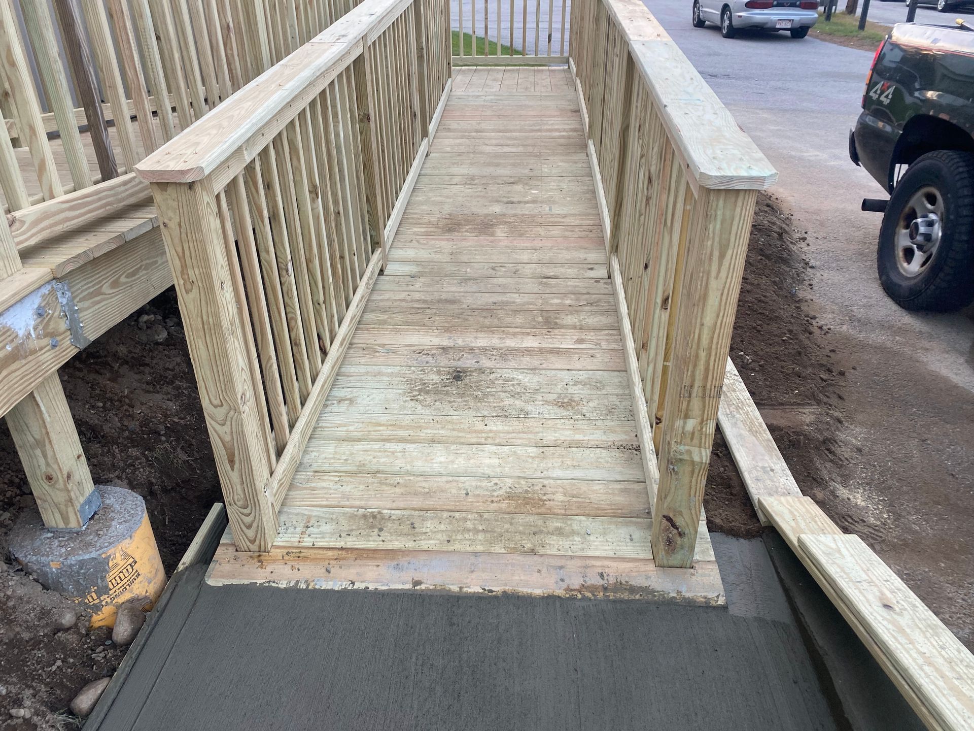 Wooden accessibility ramp with railings leading to a sidewalk beside a parking area
