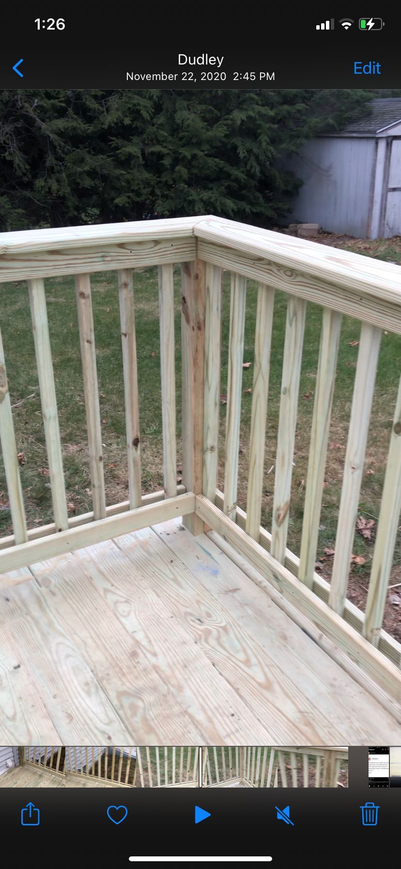 Weathered white wooden deck corner with railing, overlooking a yard and trees
