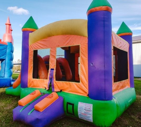 Colorful inflatable bounce house with purple, green, orange, and blue towers on grass outdoors