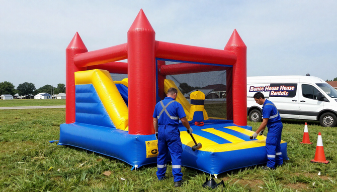 People setting up a red, blue, and yellow inflatable bounce house on a grassy field.