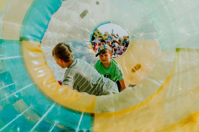 Two children inside a colorful inflatable tunnel, one in green reaching through a circular opening
